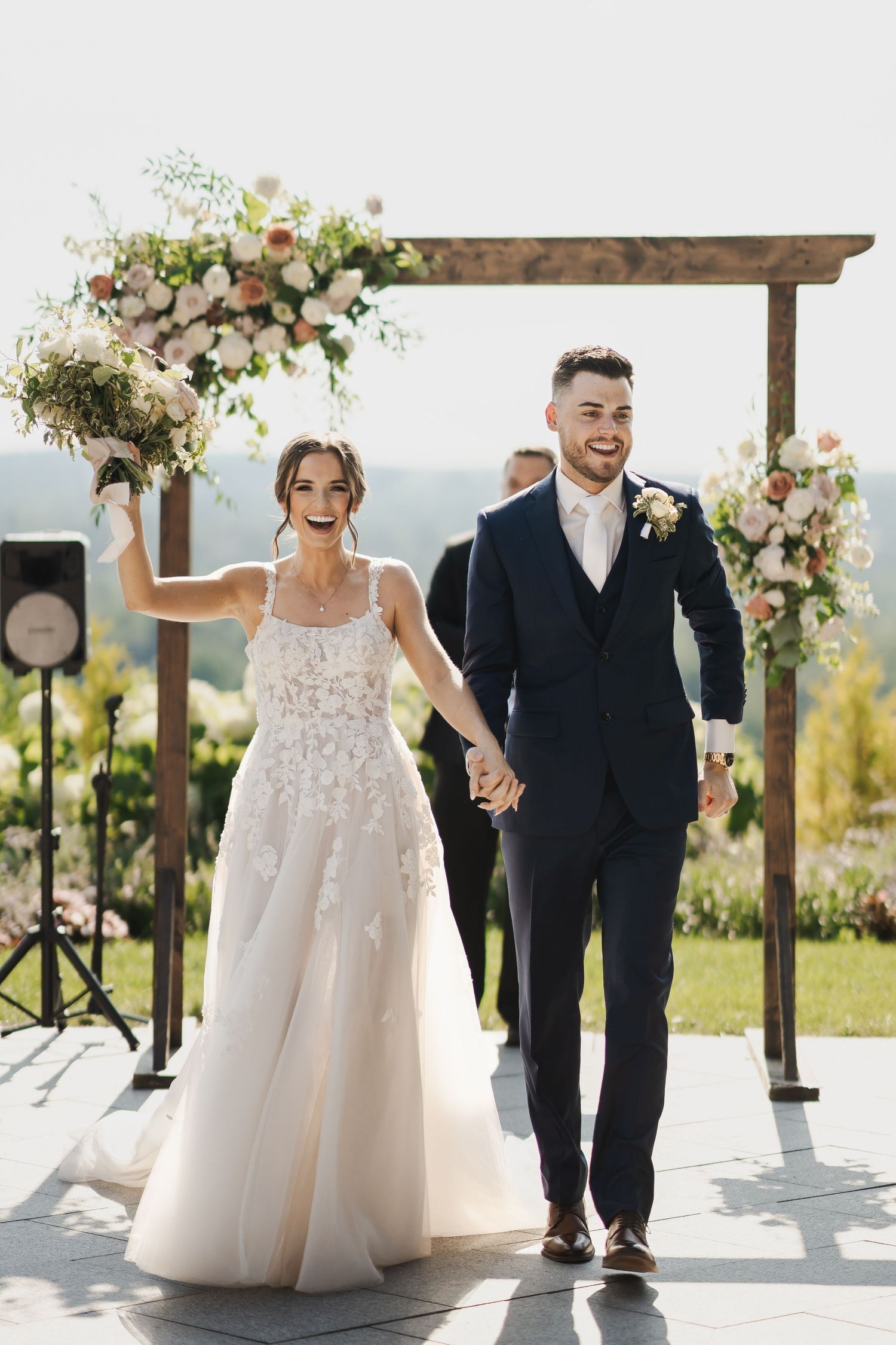 Newlyweds walk together under a floral decorated arbor on their wedding day.
