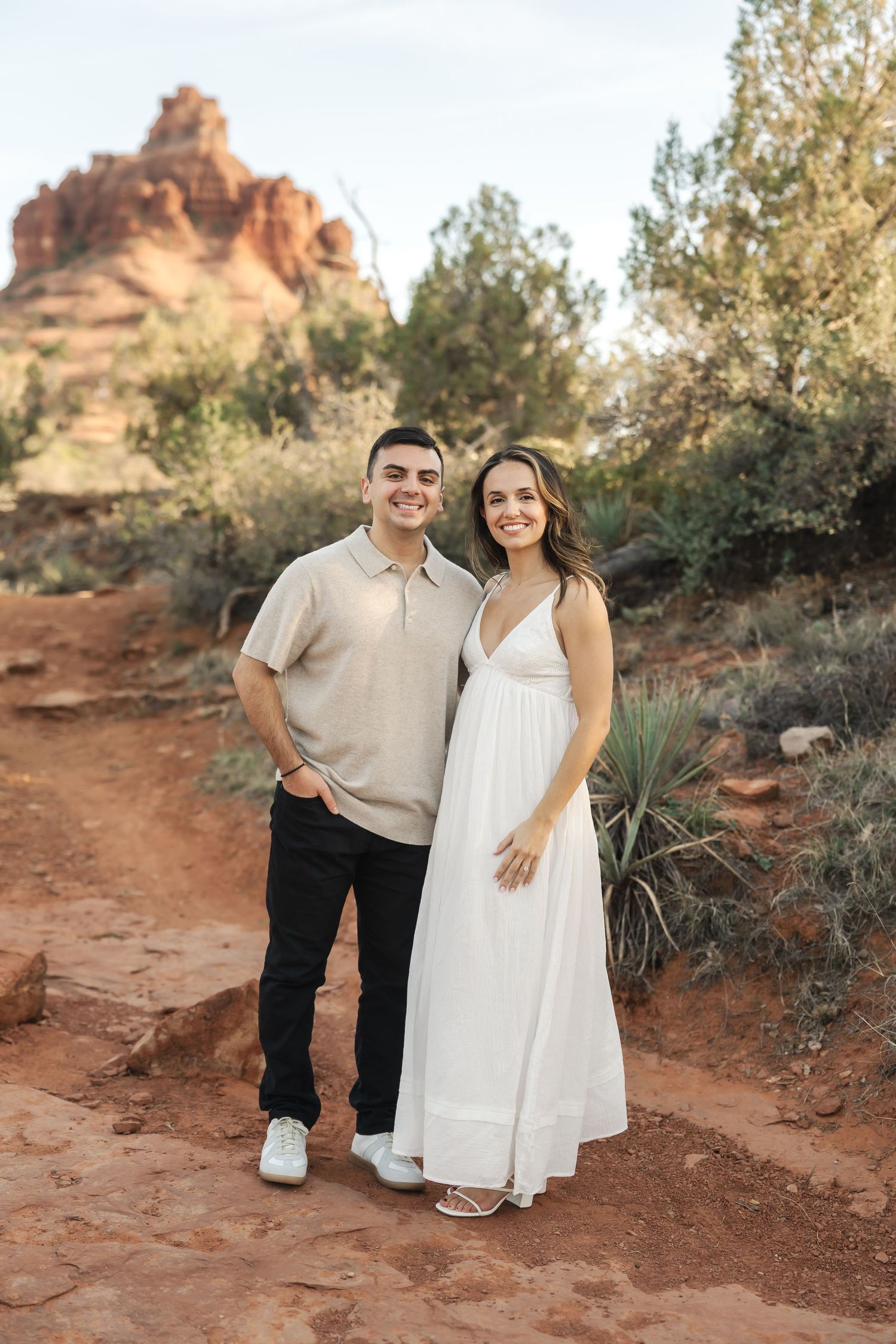 A couple poses together on desert trails with red rock formations in the background.