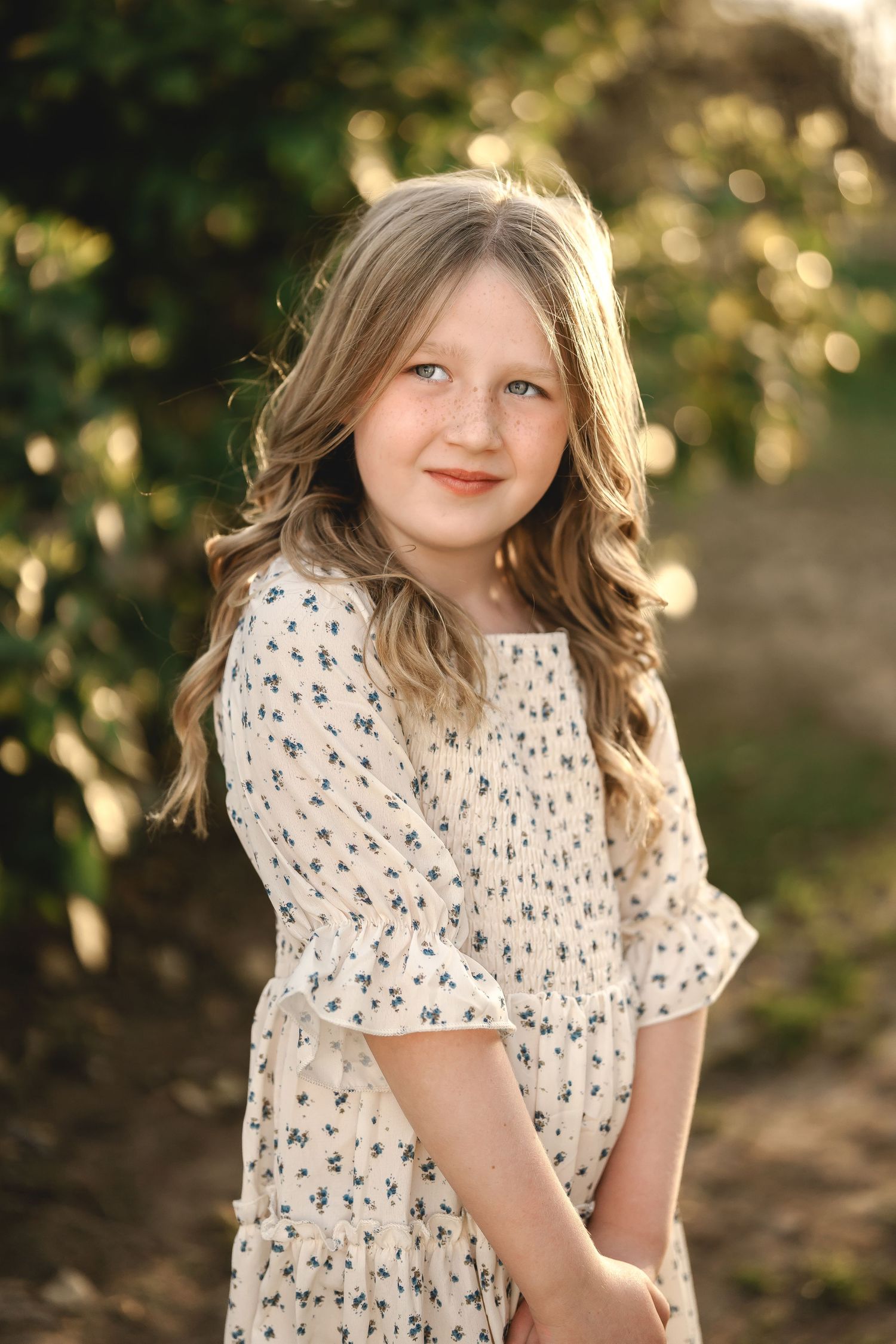 Natural light portraits capturing delicate expressions with floral dress against garden backdrop.