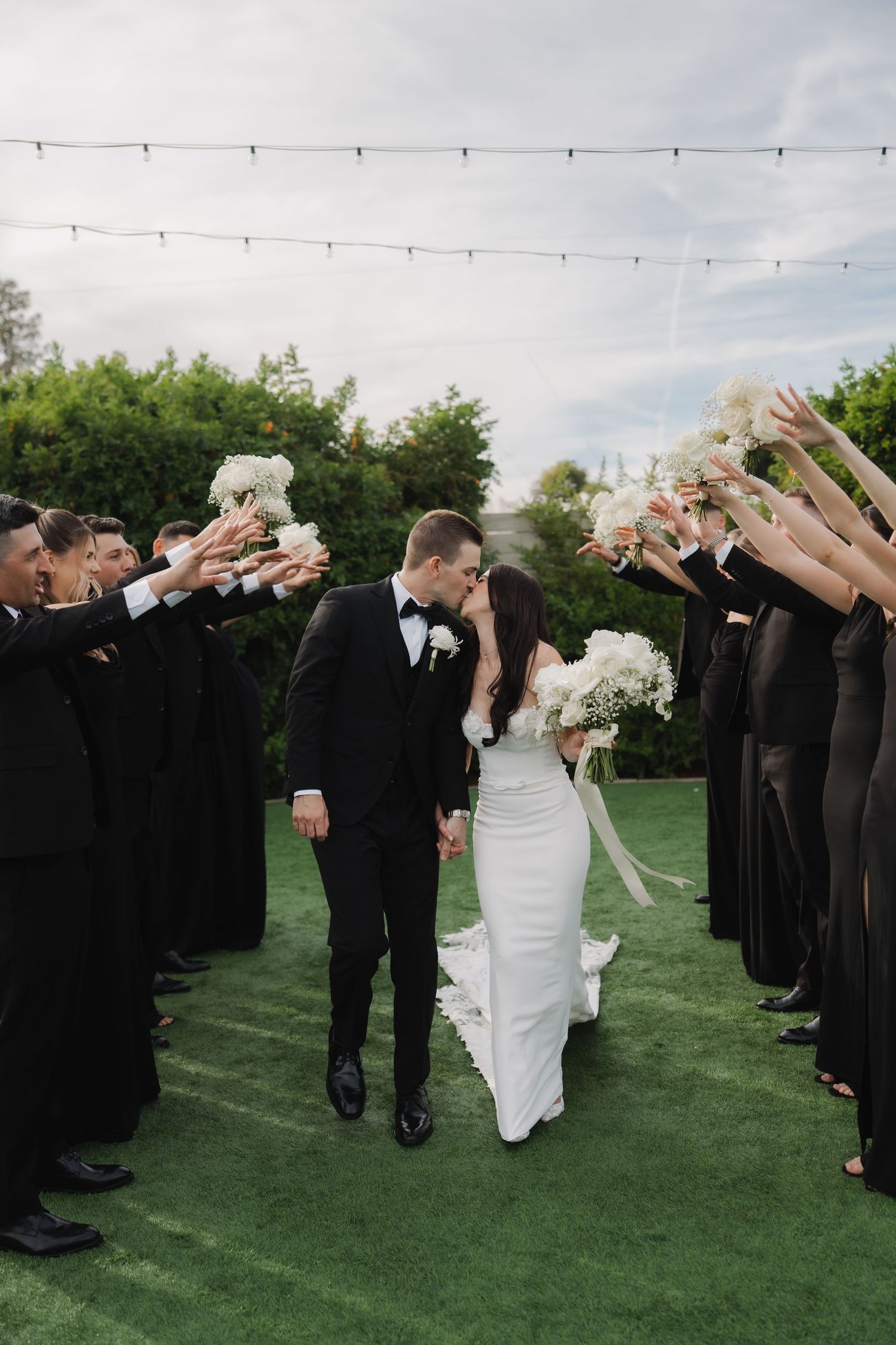 Wedding party forms tunnel for newlyweds to walk through on grassy lawn.