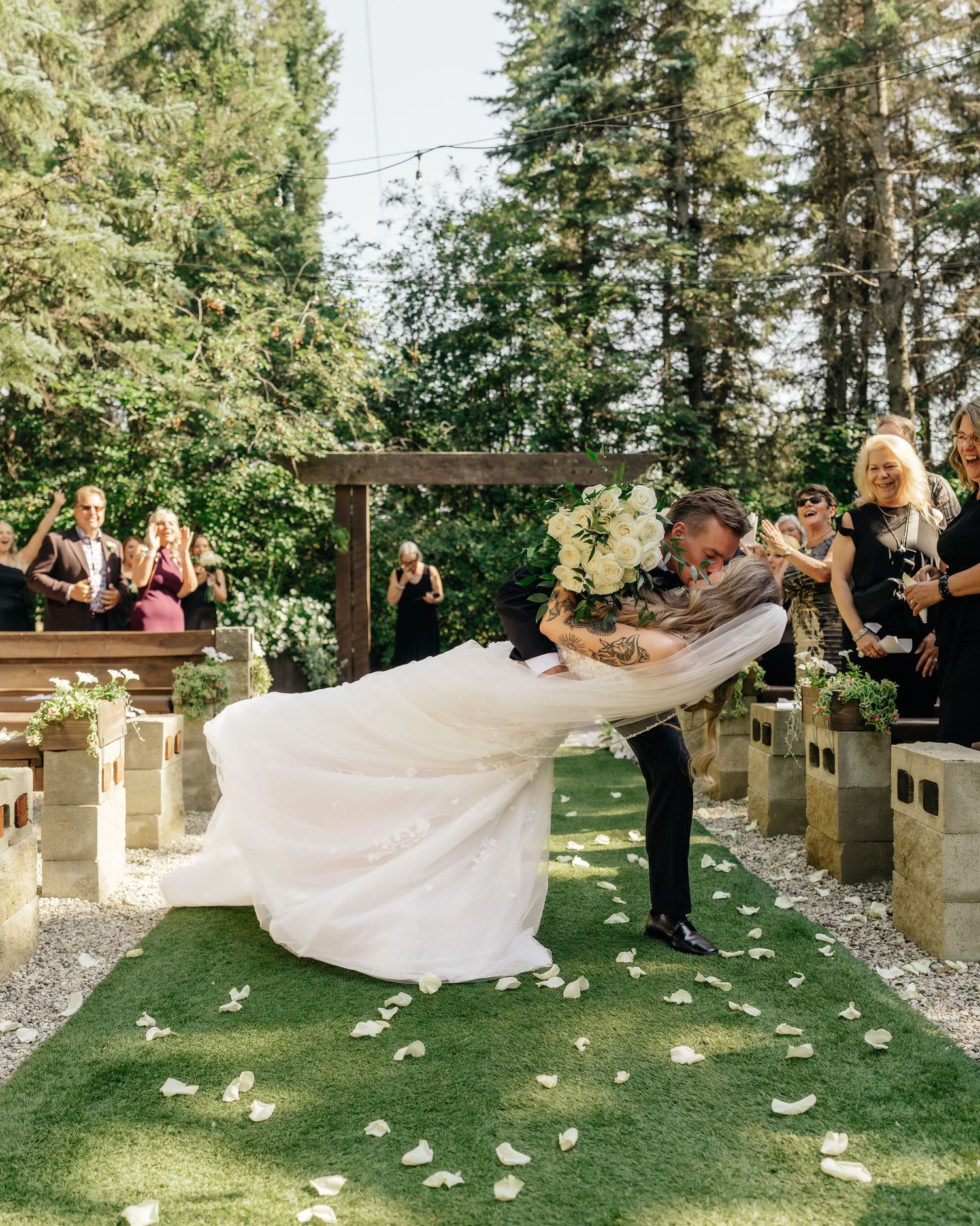 Wedding party tossing bride's veil in outdoor garden ceremony setting.