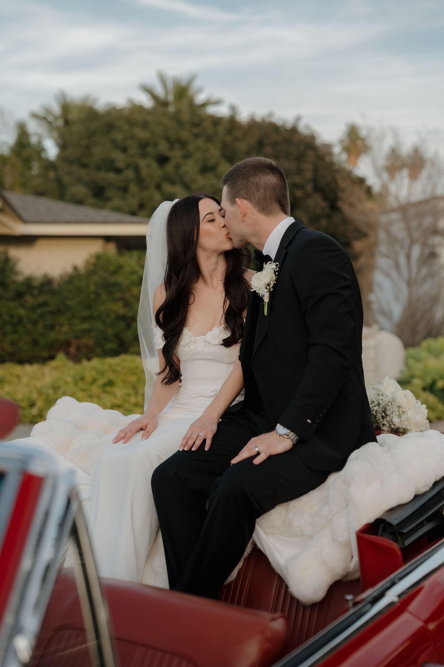 Newlyweds share romantic moments in vintage red car during their wedding day.