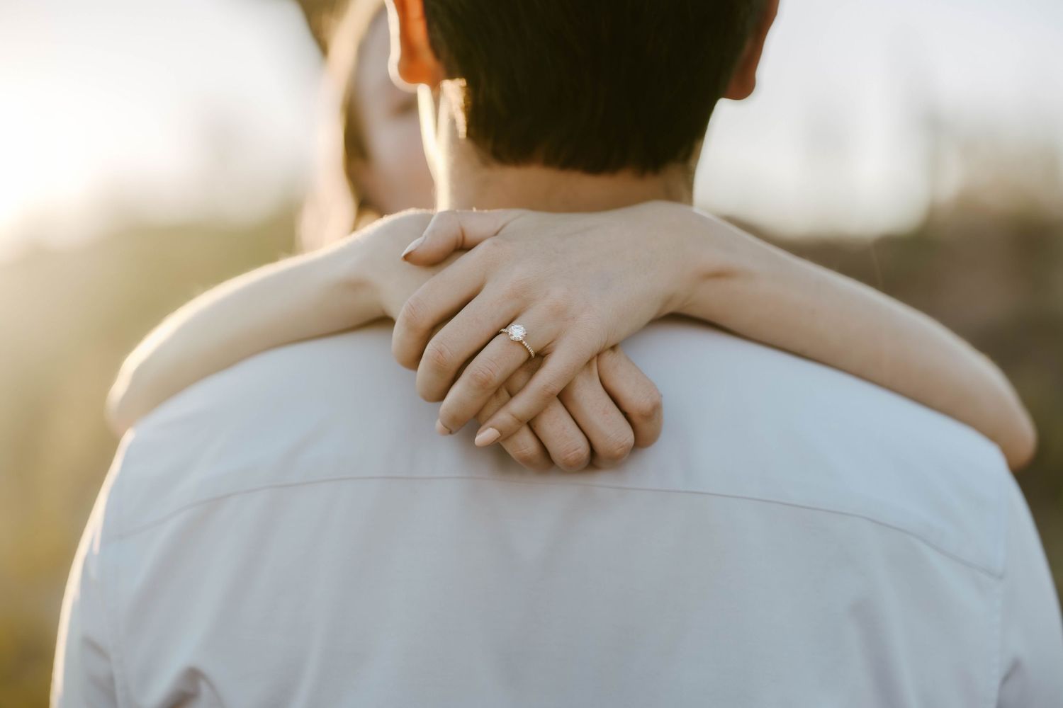 Close up of entwined hands during a romantic outdoor wedding photoshoot in soft sunlight.