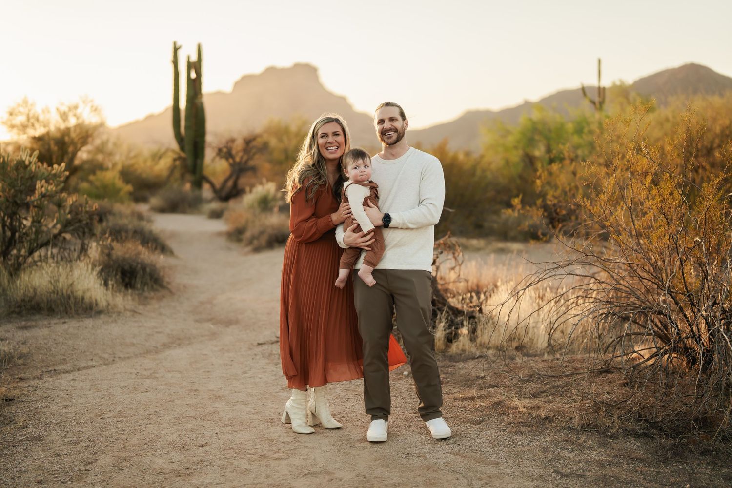 Family walking together on desert trail with saguaro cactus at sunset.