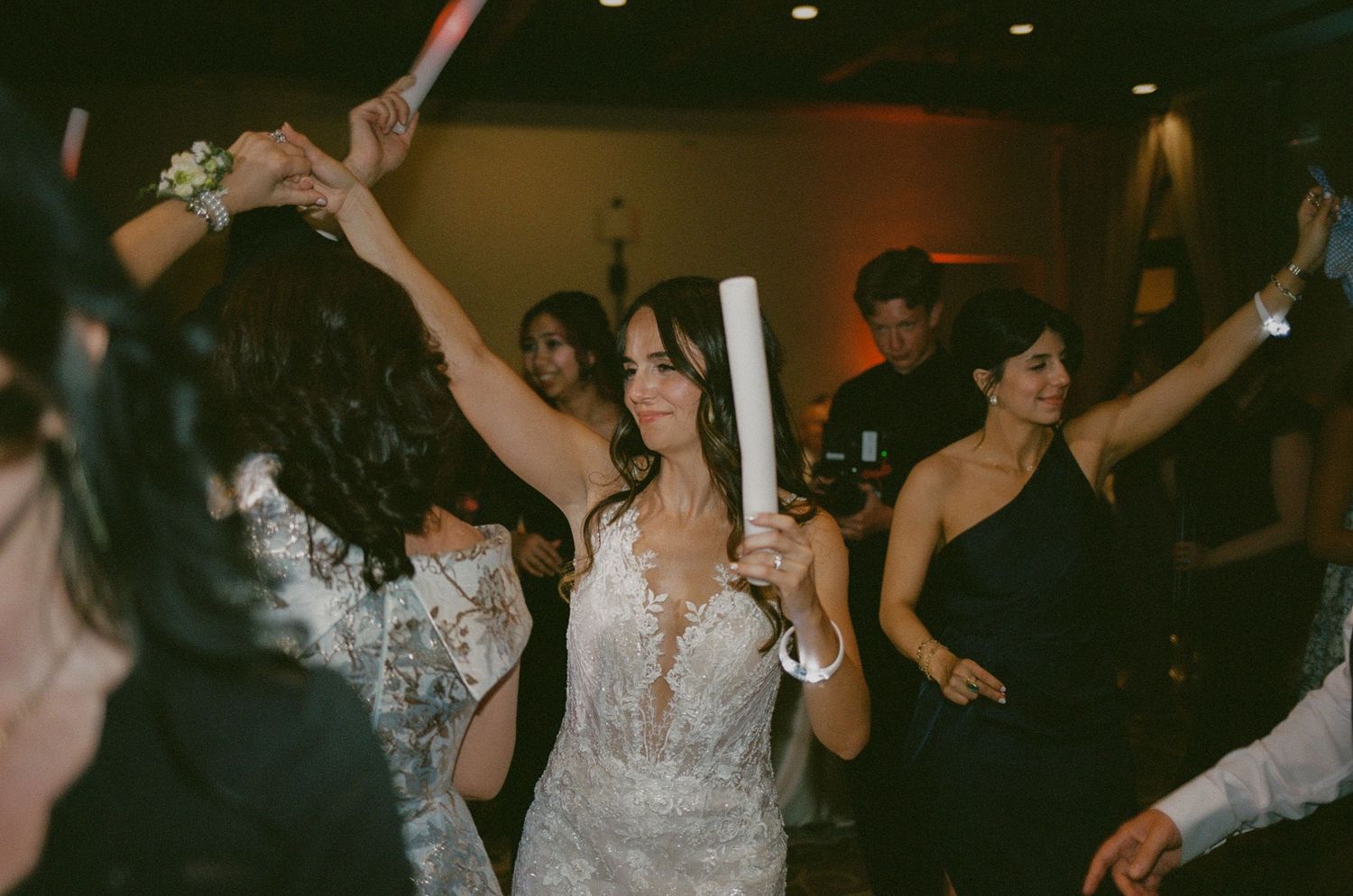 Bride in lace wedding dress dancing joyfully with guests at a lively wedding reception party.