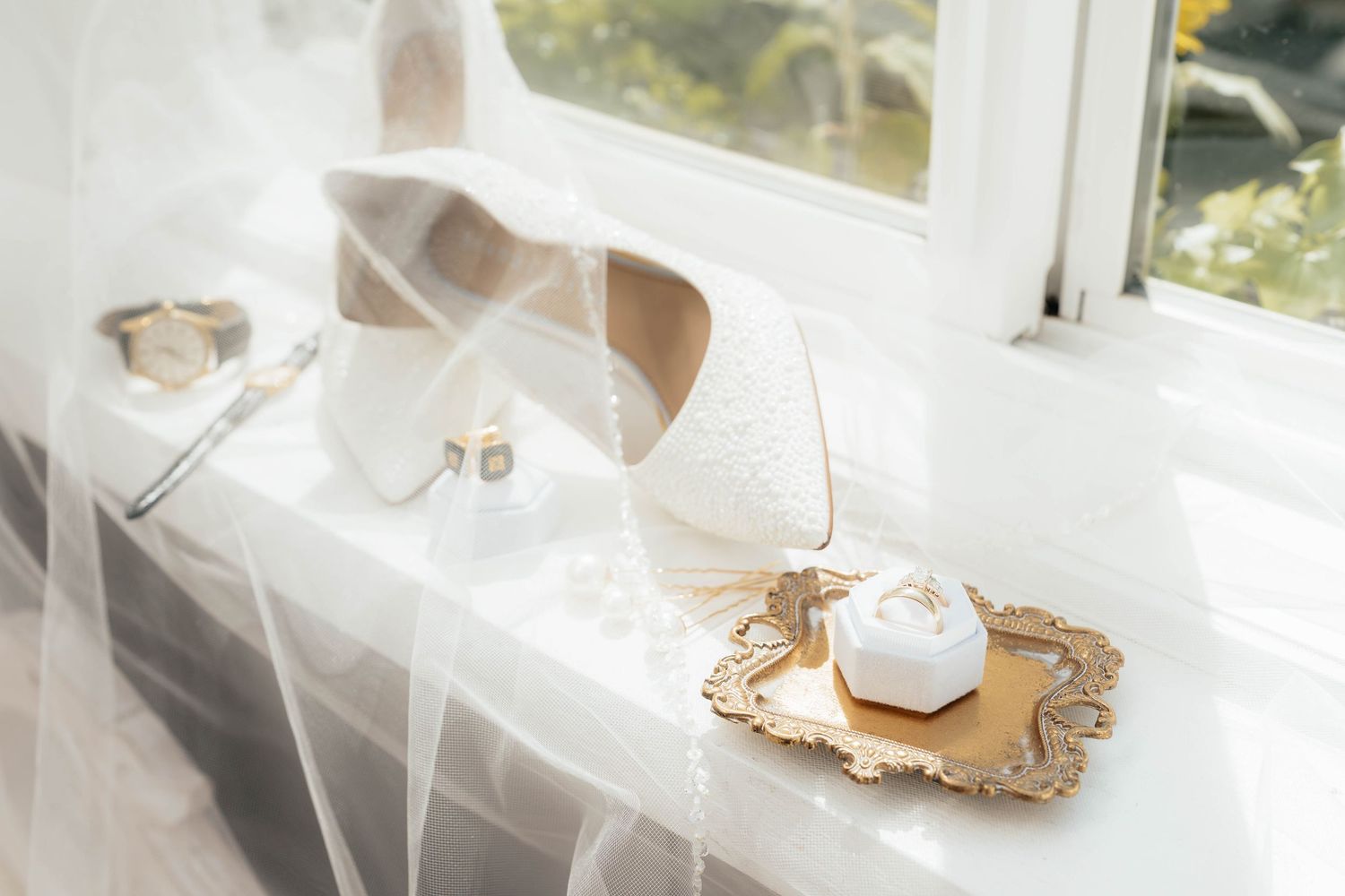 White wedding dress and veil arranged on an elegant vintage mirror tray with natural light streaming through windows.