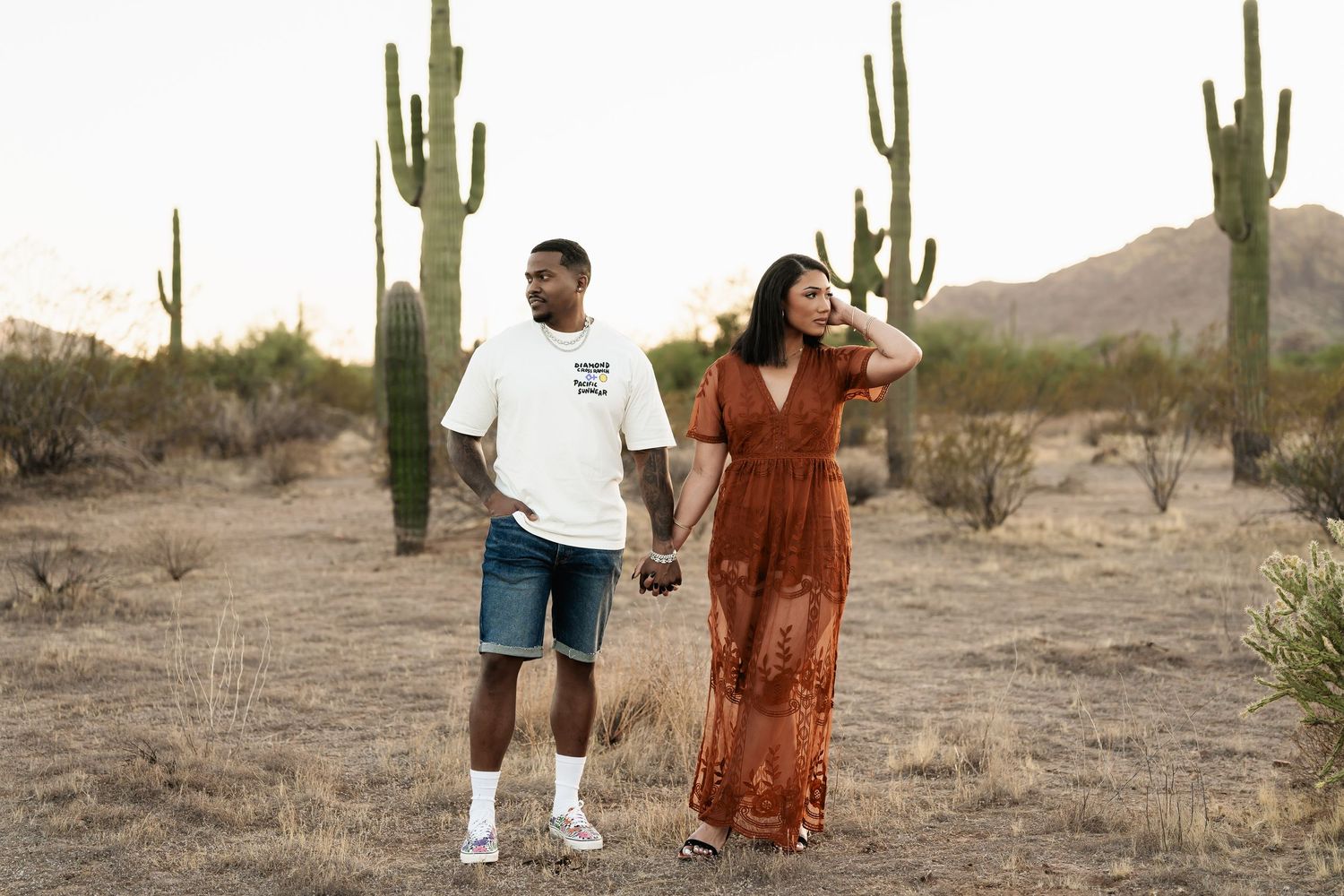 A couple poses playfully among tall saguaro cacti in the Arizona desert.