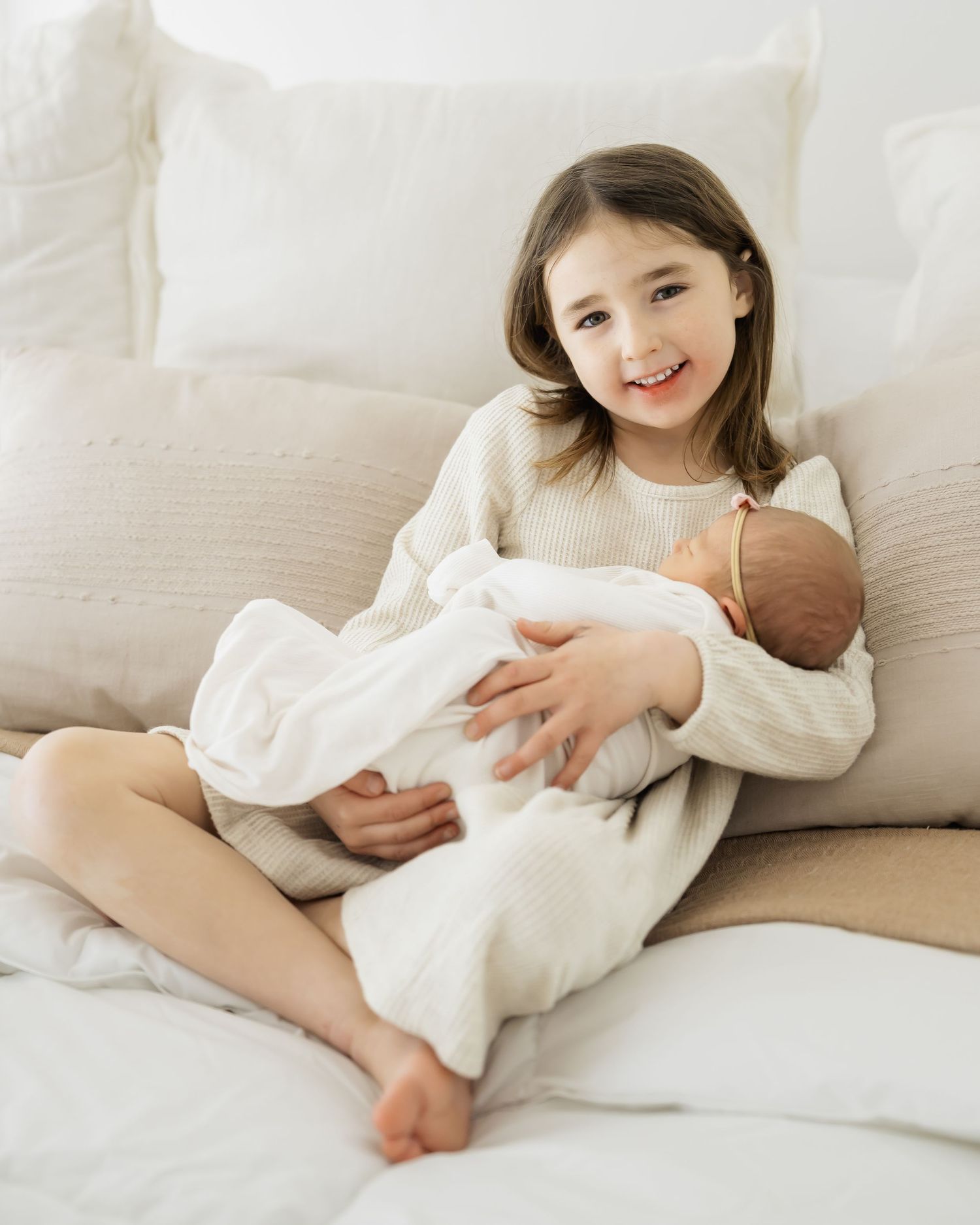 Child relaxing on white couch in cream colored sweater during indoor photo session.
