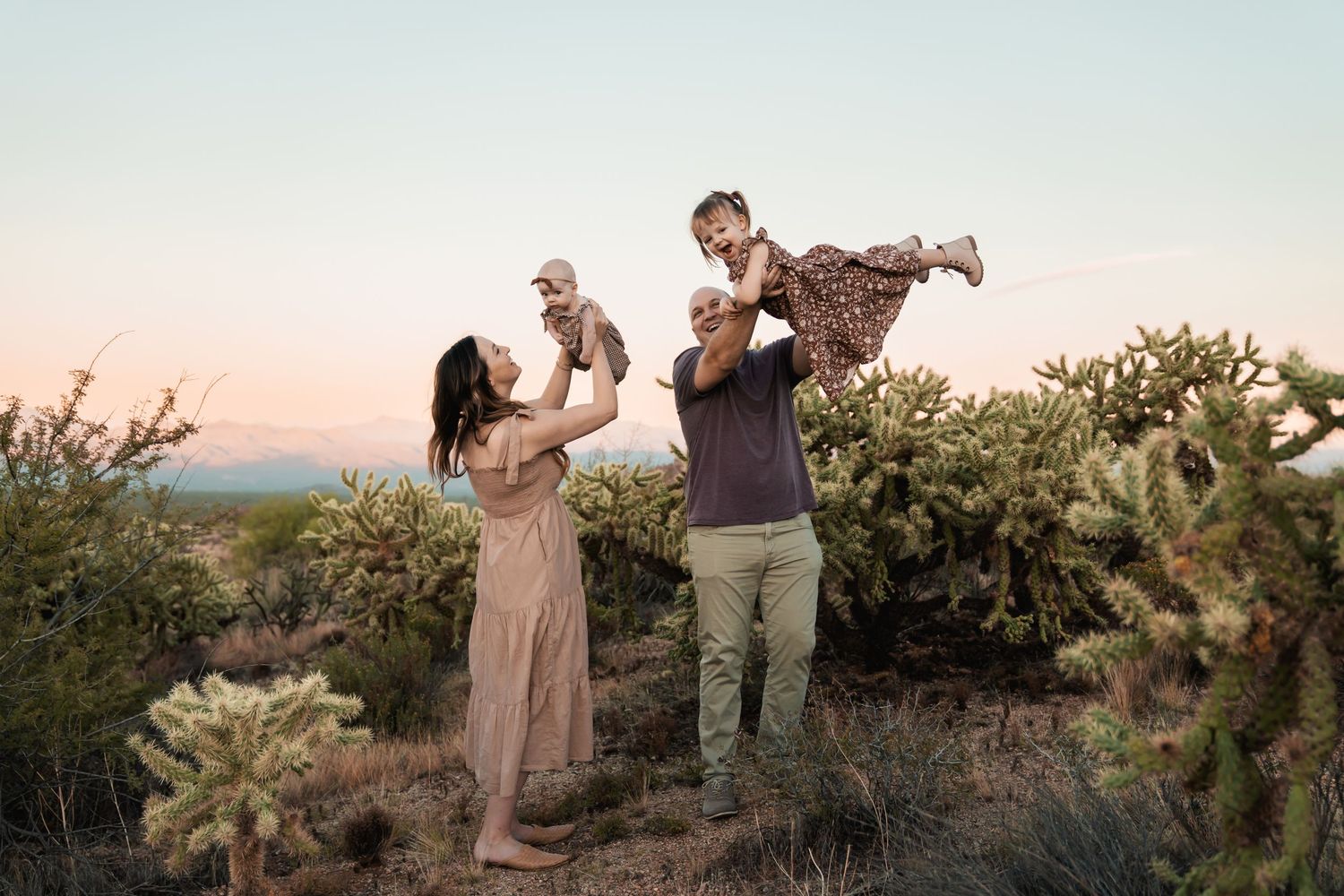 A romantic desert engagement photoshoot at sunset with desert plants and mountain scenery in the background.