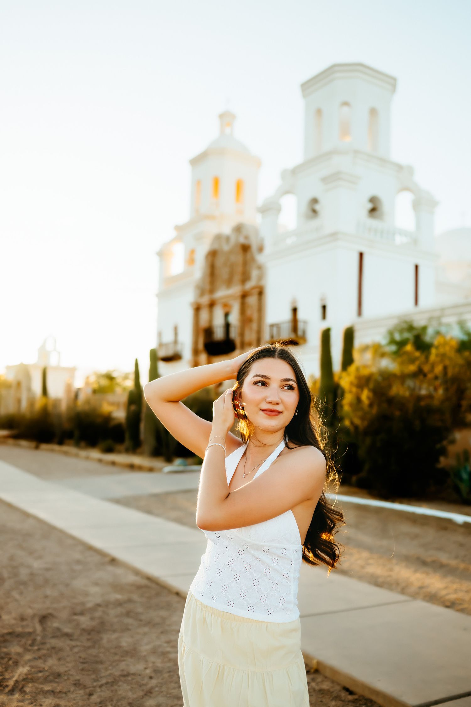 Senior girl in front of a white church in Tucson, Arizona, with a white top and a yellow skirt.