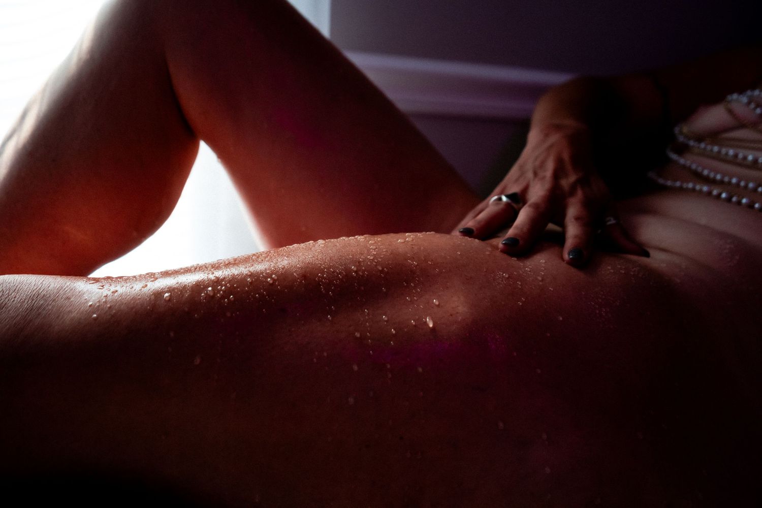 Shiny water droplets form abstract patterns on wet skin in dramatic lighting conditions.