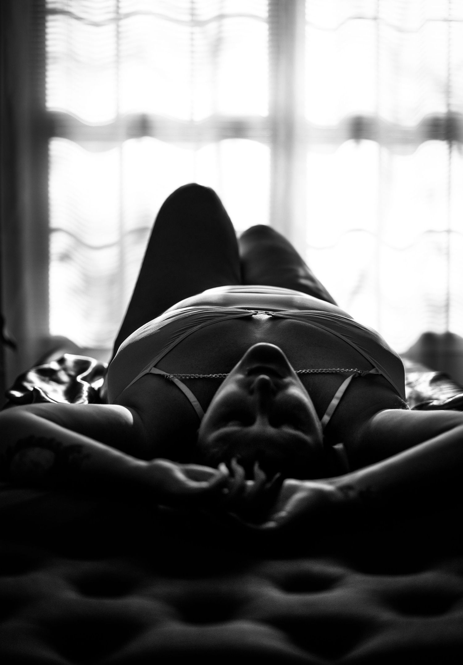 A black and white artistic photograph of a silhouetted figure resting on dark textured bedding.