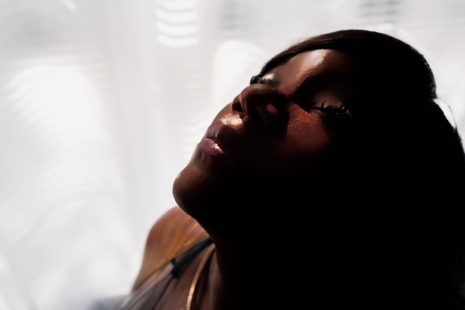 A person with closed eyes and upturned face against a dark background in a contemplative pose.