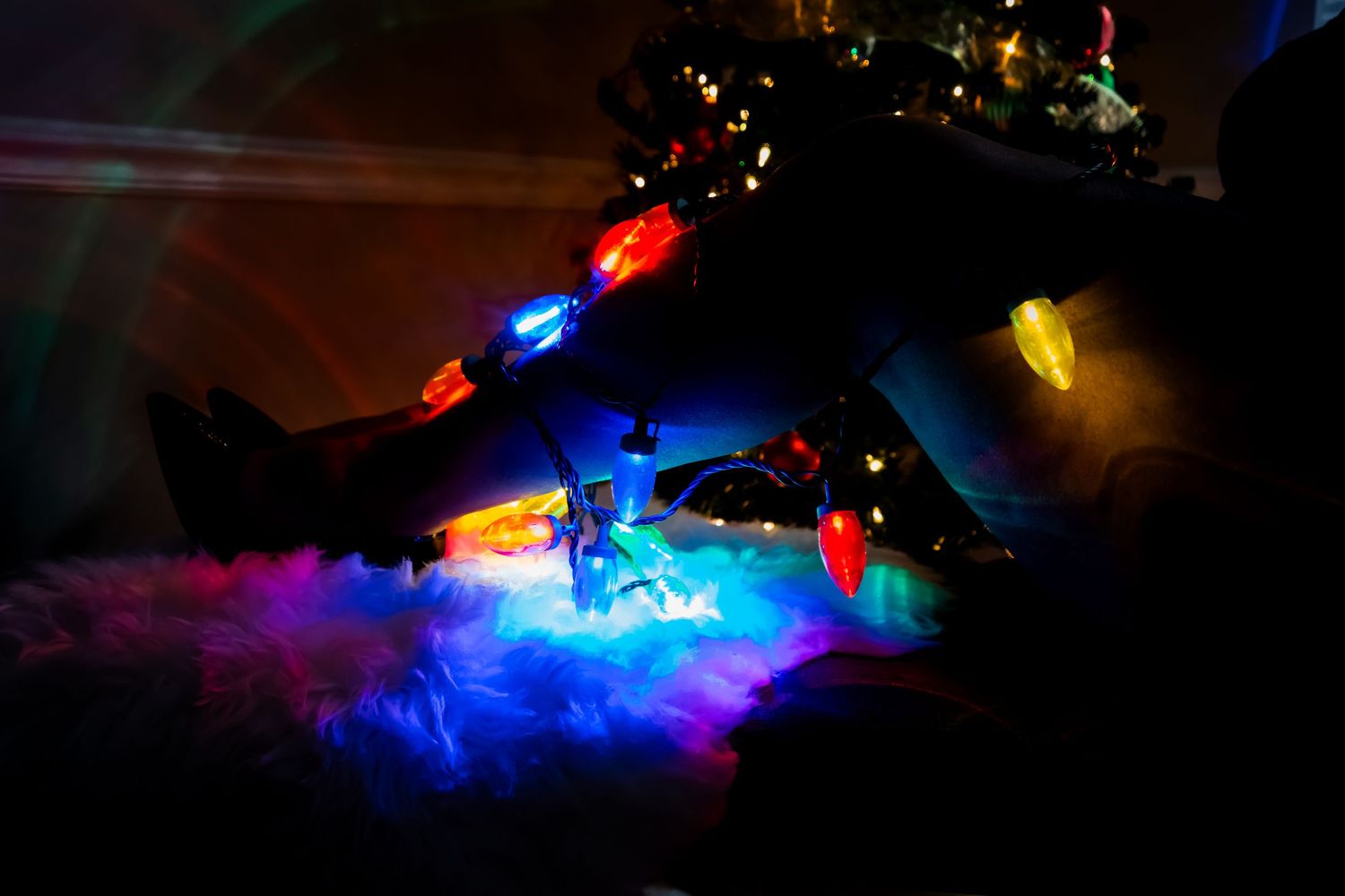 Colorful Christmas lights illuminate a dark room creating glowing blue and pink reflections on the floor.