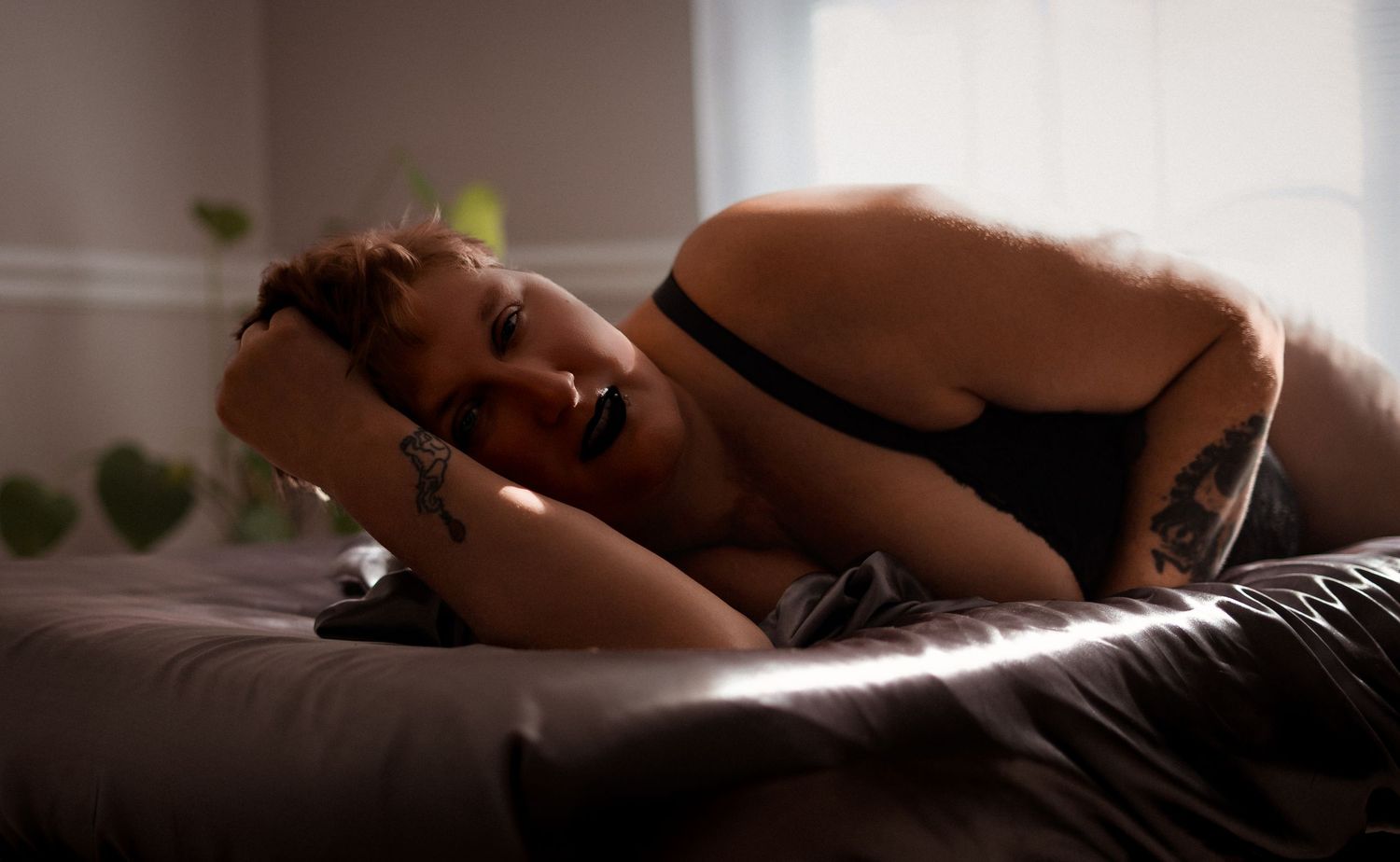 Intimate couple holding hands while lying together on bed in soft morning light.