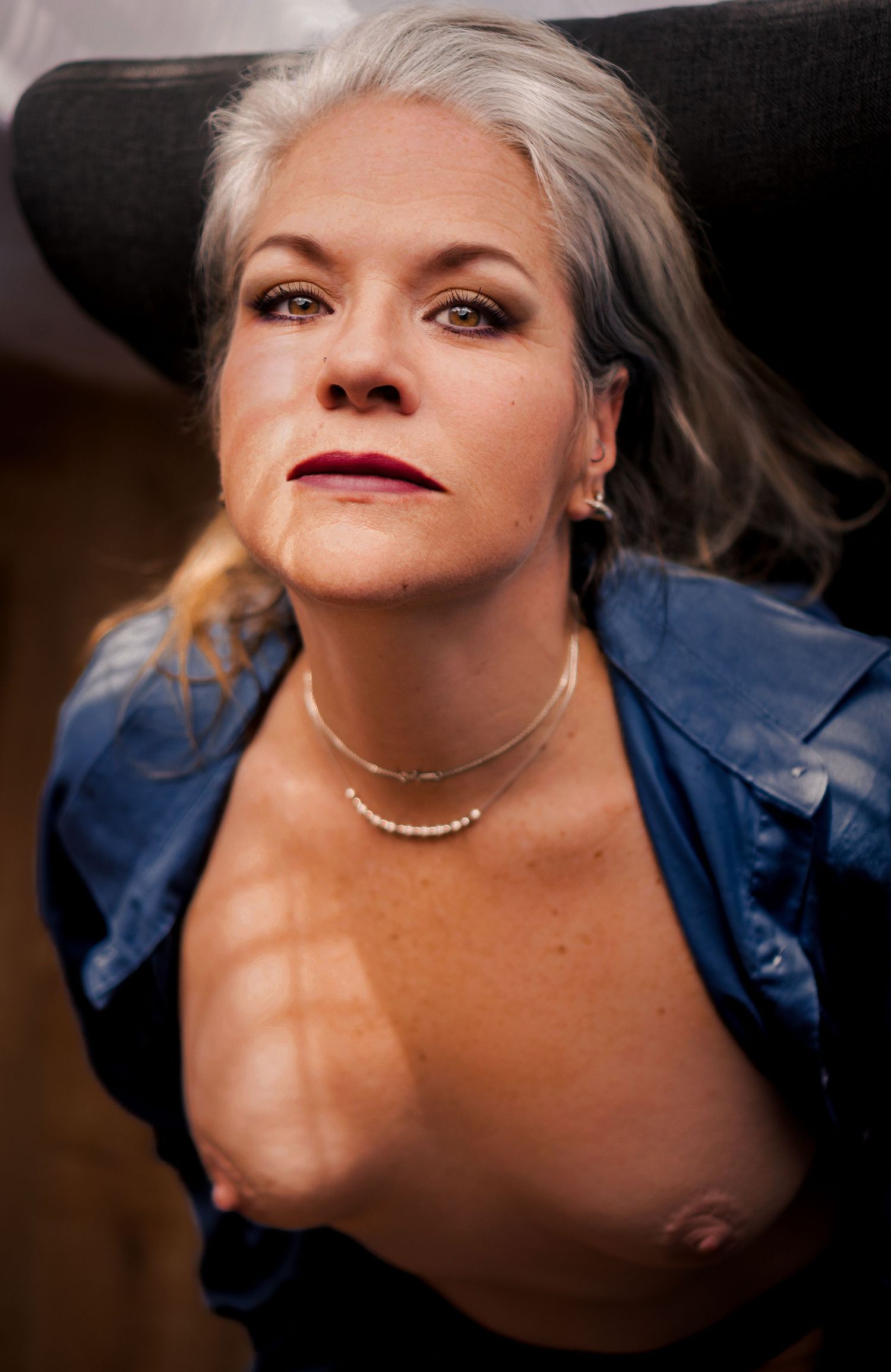 A person wearing a blue denim jacket is photographed from below with dramatic lighting and dark lipstick.