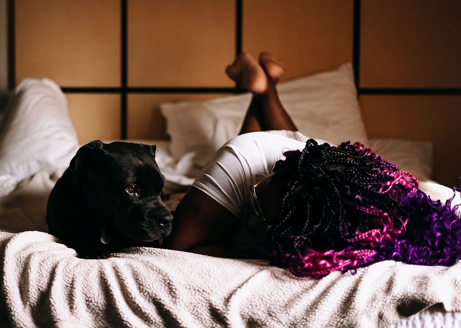 Person resting on white bedding illuminated by purple light while lying on their side.