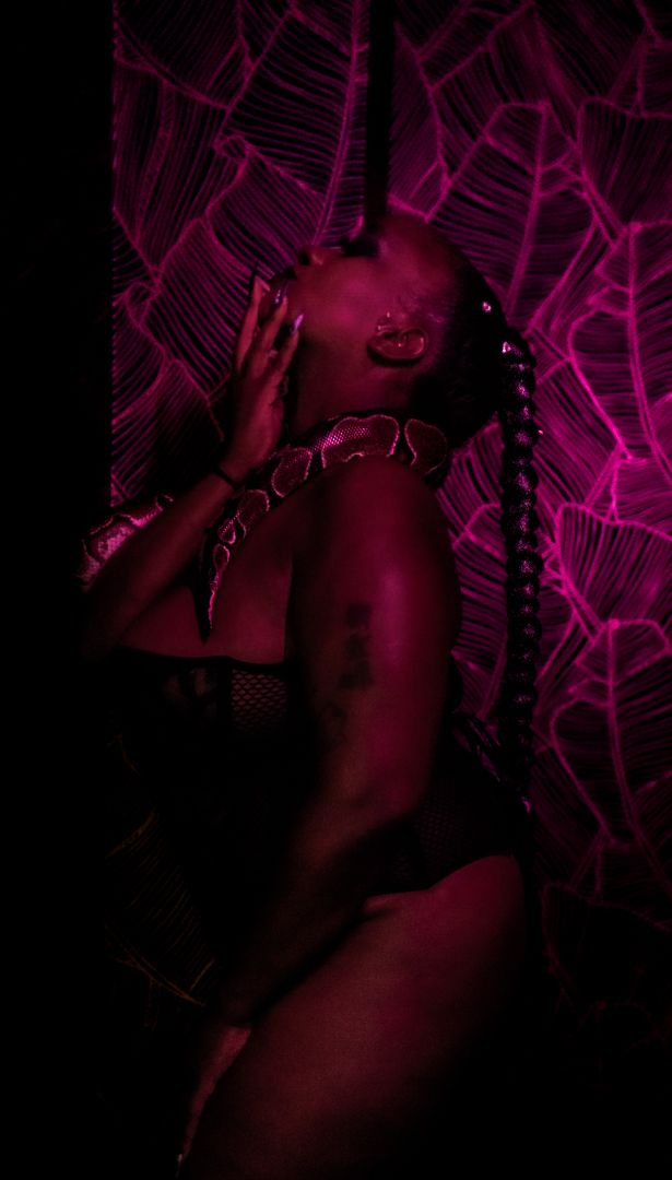 Artistic purple and magenta tinted portrait in dark lighting against geometric pattern background.