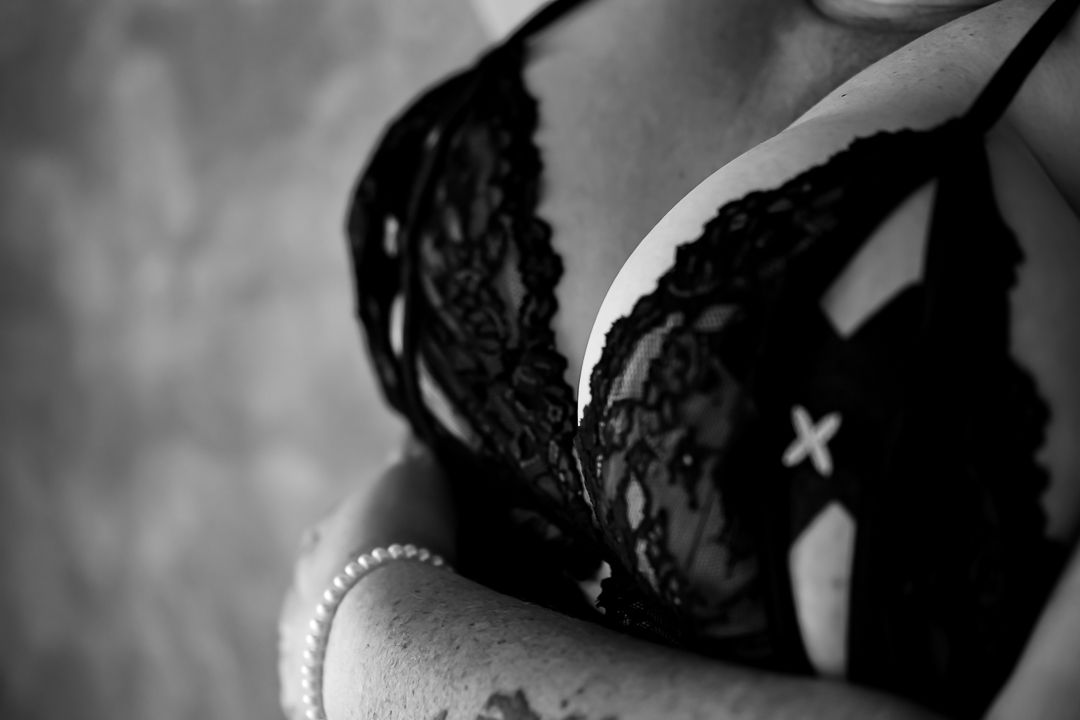 Close-up black and white photo of delicate black lace bra over skin with soft lighting.