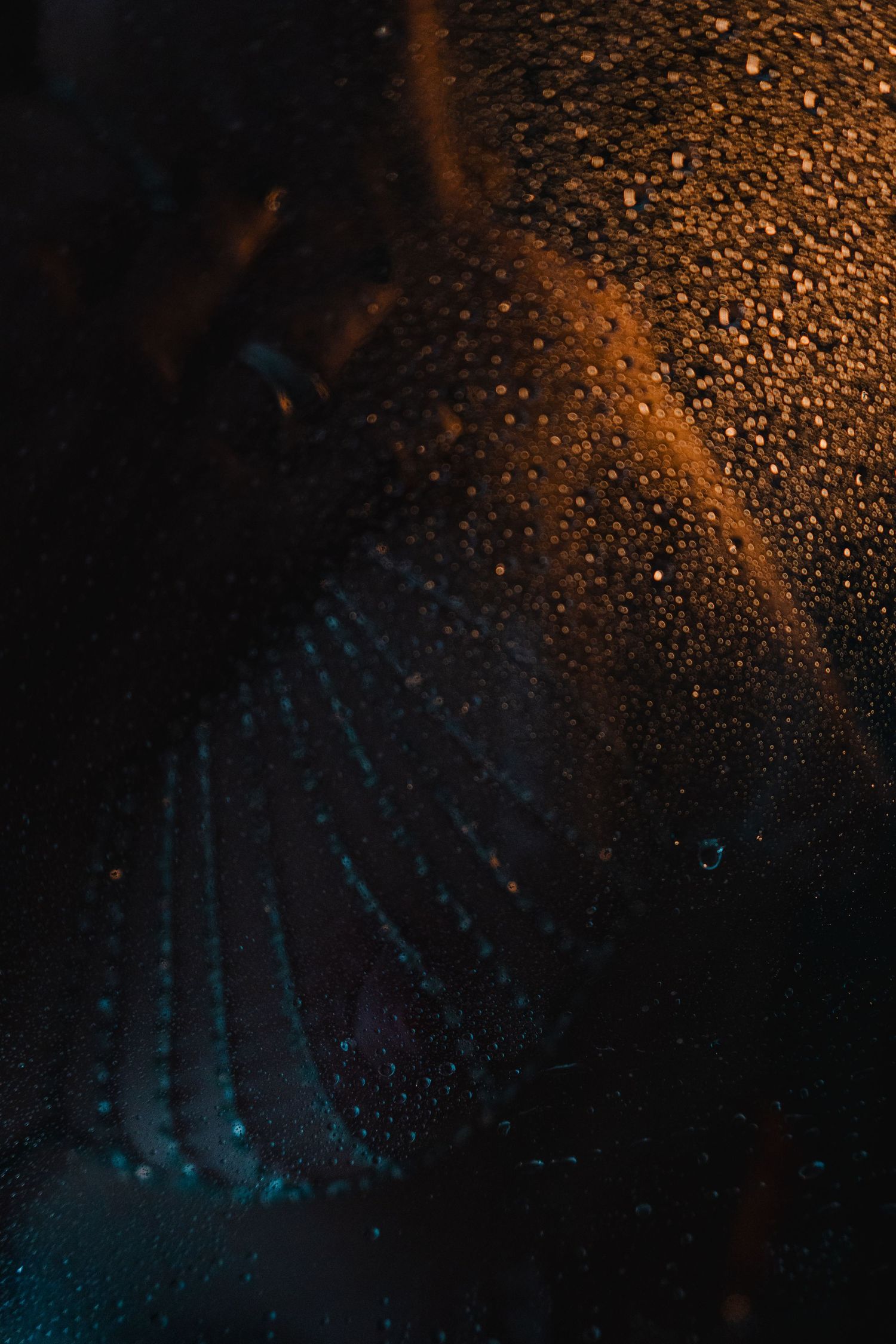 Abstract dark background with water droplets reflecting orange and turquoise light creating a moody atmosphere.