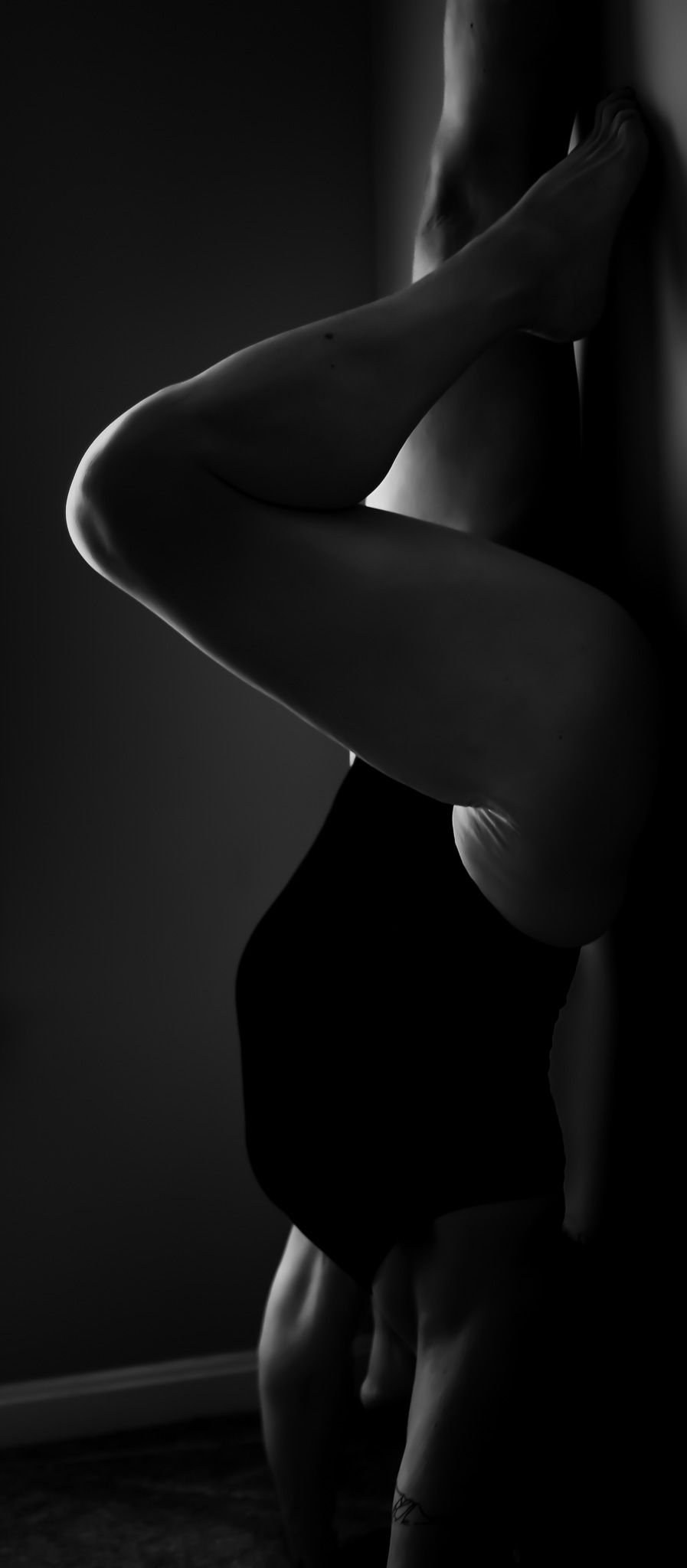 Black and white artistic nude photograph showing silhouetted curves and shadows in dramatic lighting against dark background.