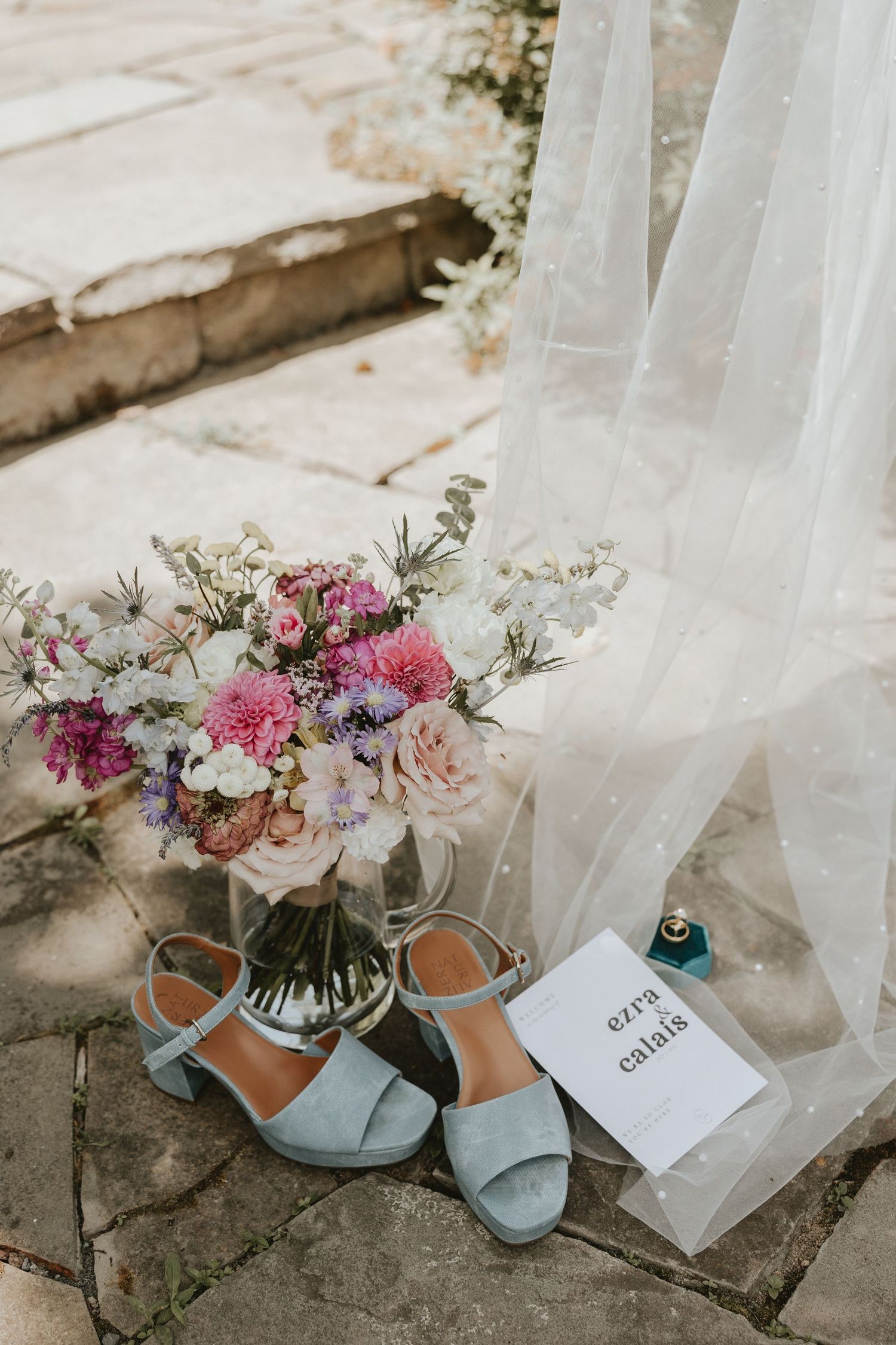 Elegant blue wedding shoes displayed with pink and white floral bouquets and delicate white tulle fabric.