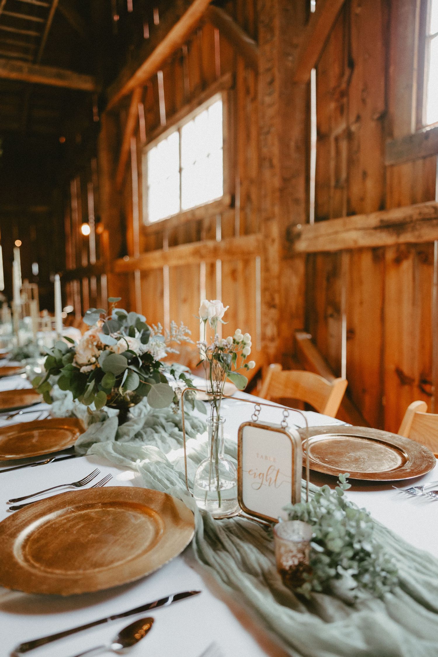 Rustic barn wedding reception table settings with wooden charger plates and delicate eucalyptus garland decorations.