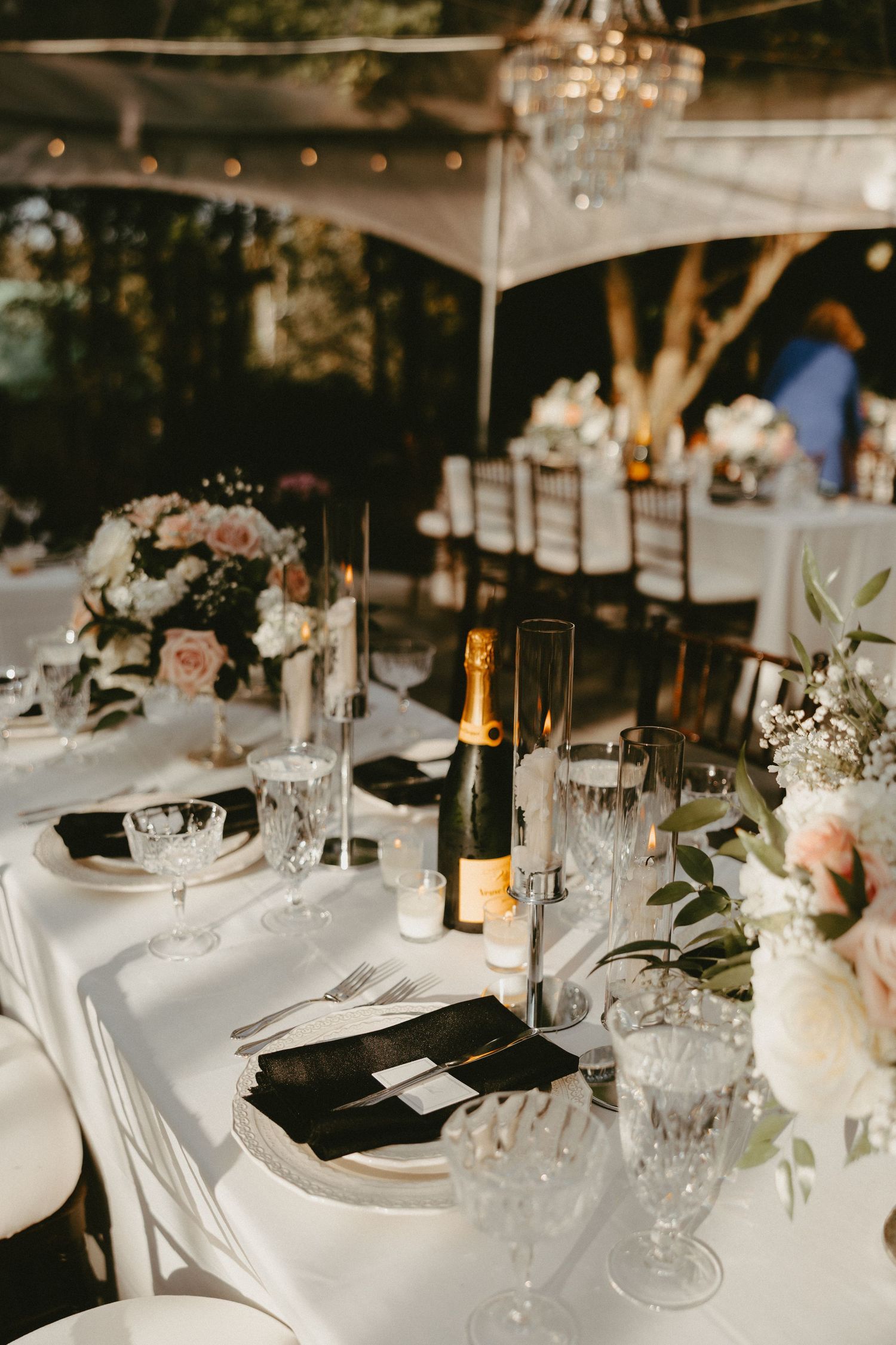 Elegant wedding reception table setting with white linens, crystal glassware, black napkins and romantic floral centerpieces.
