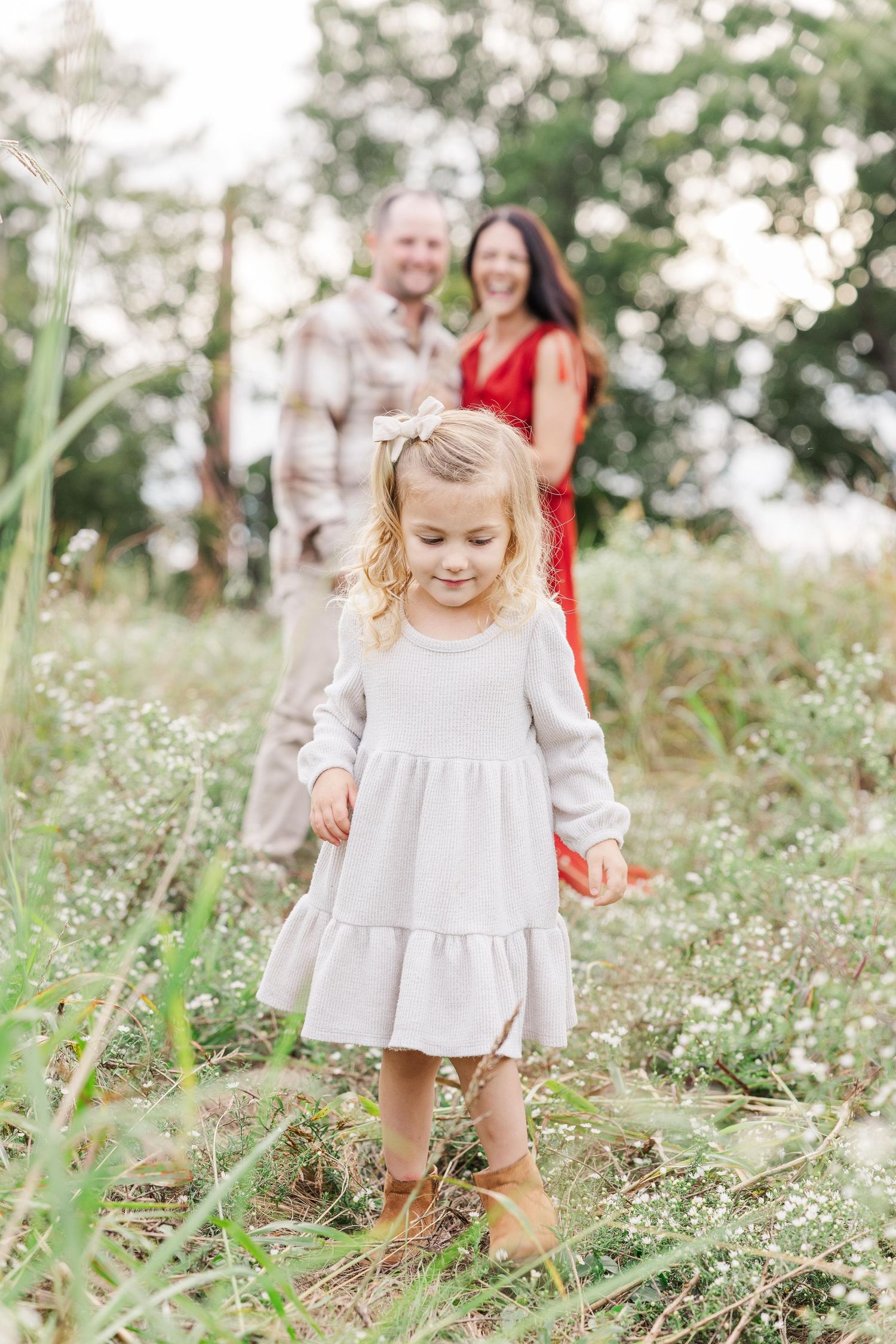 Young child in a light dress explores the NC Art Museum wildflower field in Raleigh while mom and dad look on in the background.