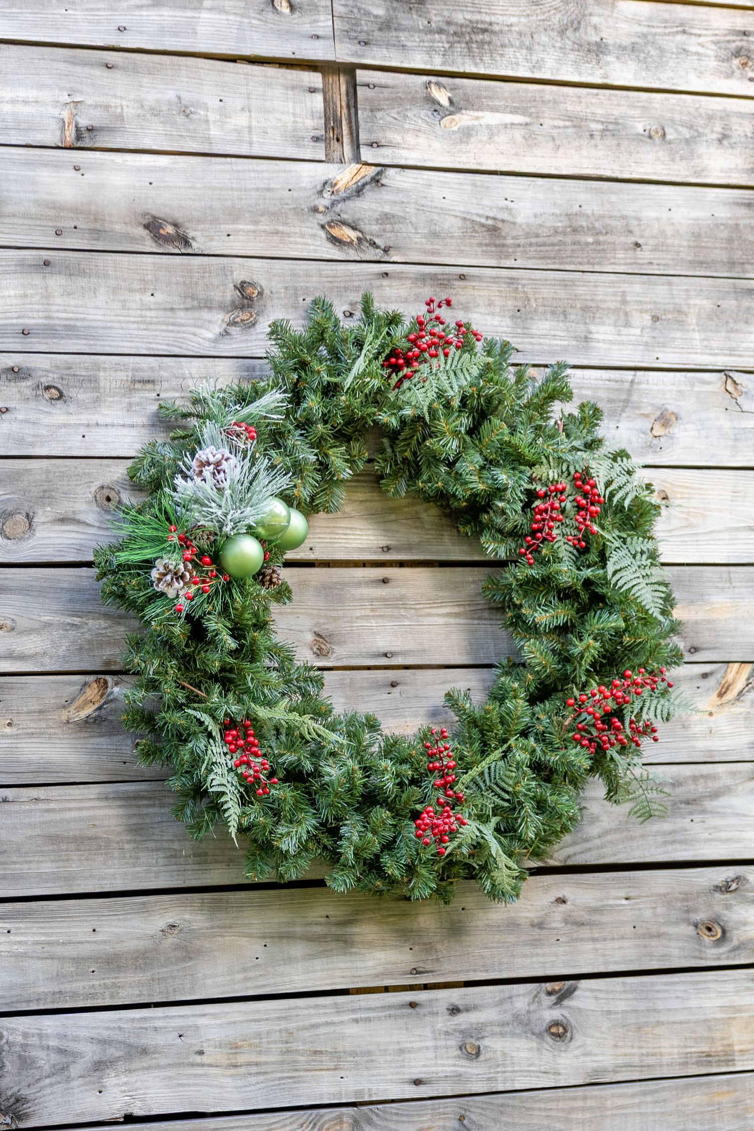 Christmas wreath with red berries and green ornaments hanging on a rustic wooden wall.