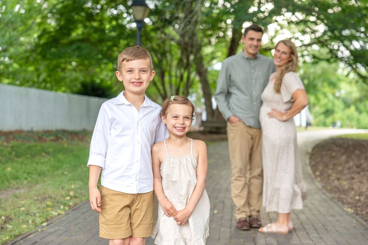 A family poses together outdoors in coordinated neutral outfits on a tree-lined path during a spring photo session in Raleigh.