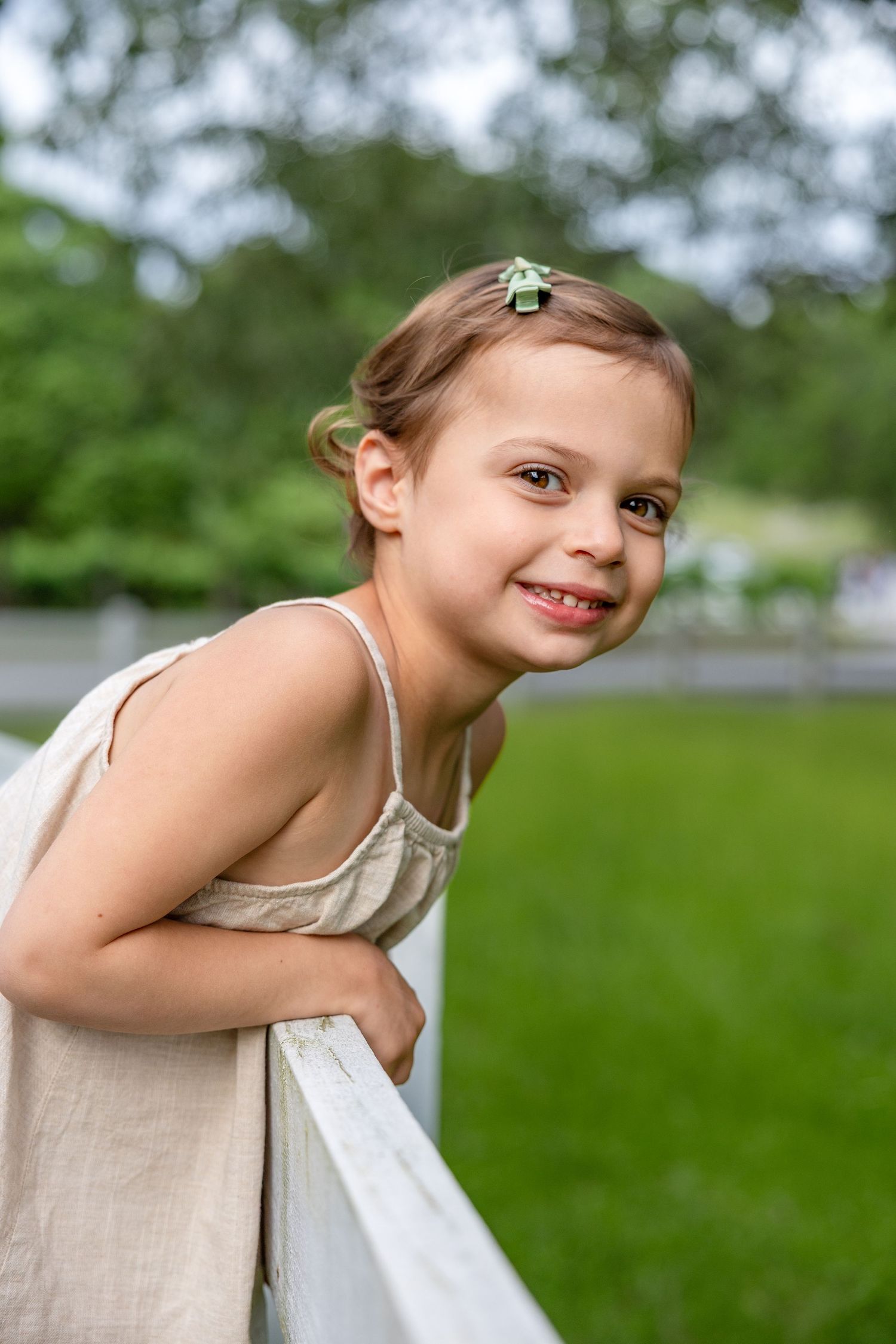 Raleigh children's photographer - portrait of a young girl with short hair and tan tank top dress leaning over a white fence.