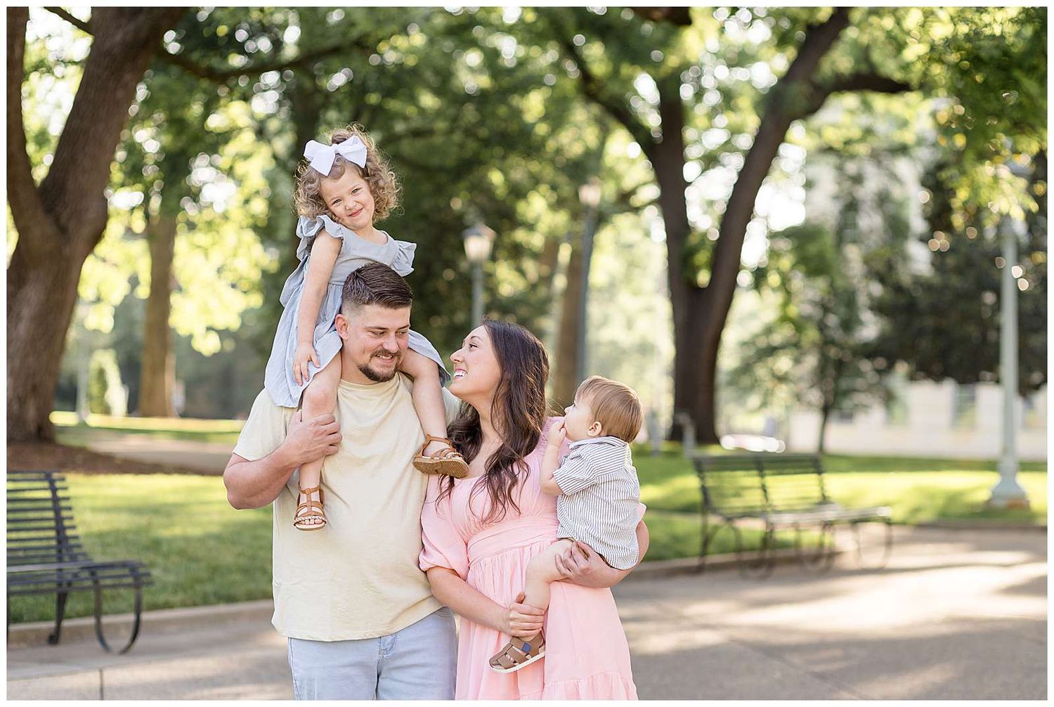 Happy family of four posing outdoors in a sunny park, parents smiling with two young children in a candid moment at the Capitol Building