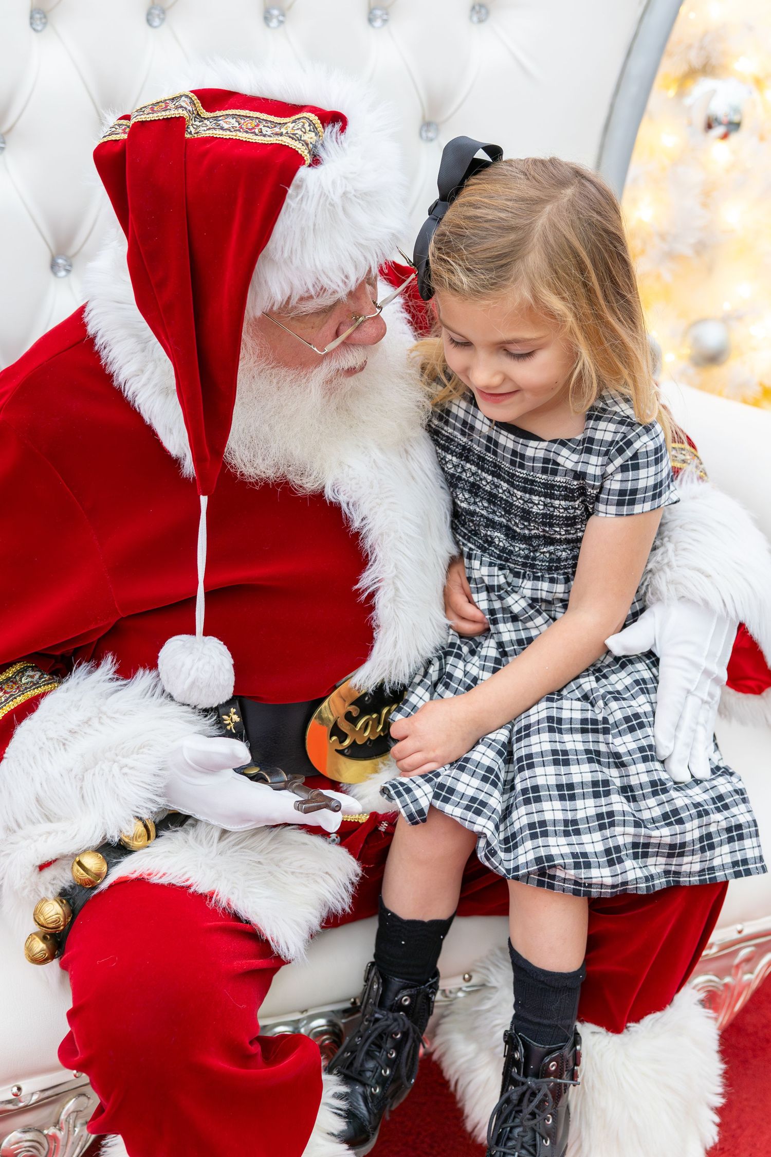 Young girl in plaid dress sitting on Santa Claus lap during a festive Christmas photo session in Cary, NC