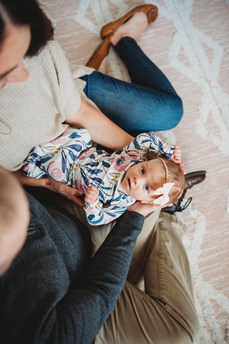 Baby wearing floral onesie lies on laps.