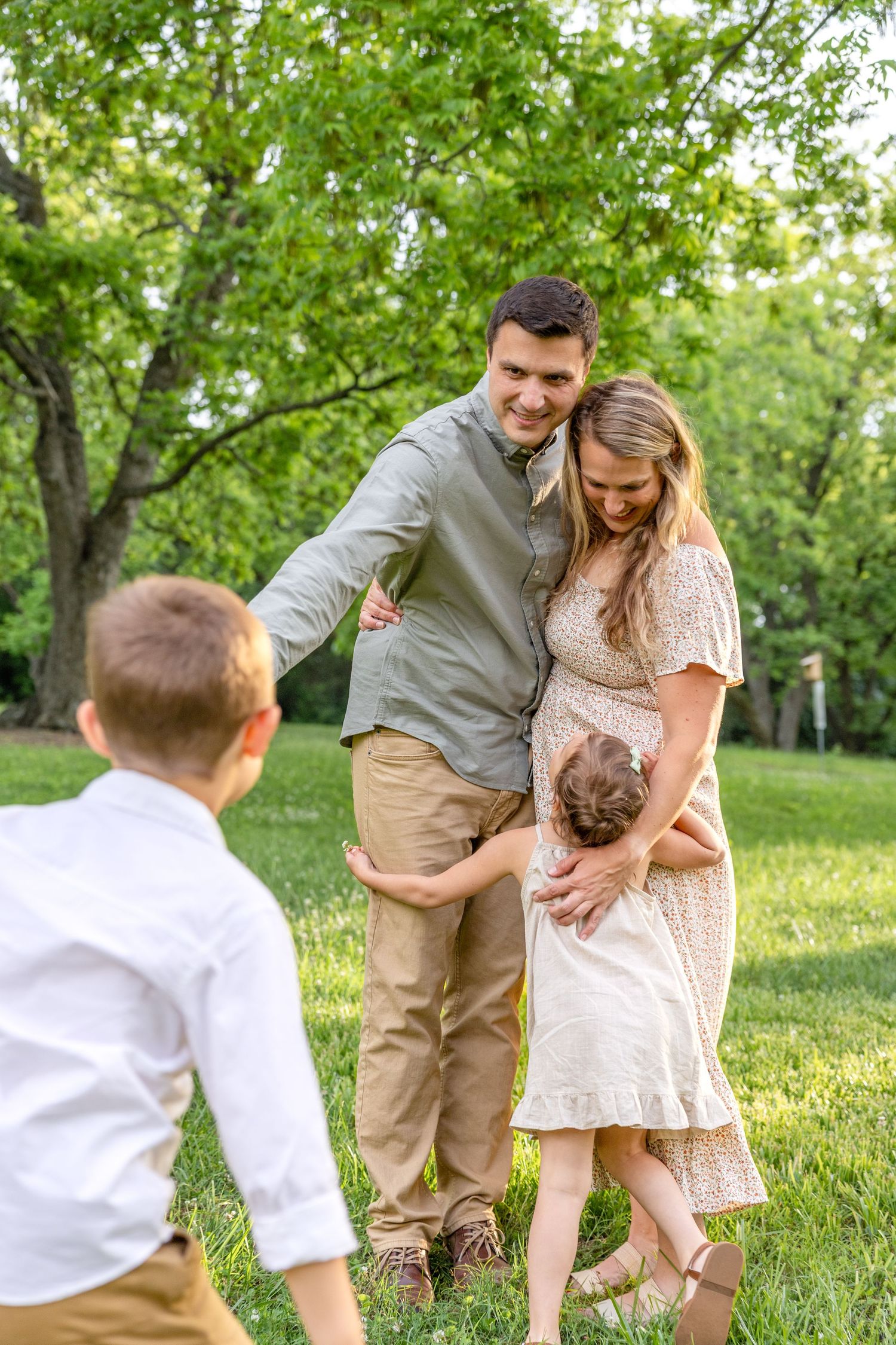 Family enjoying playful moments together in a sunny green park during a spring afternoon photo session.