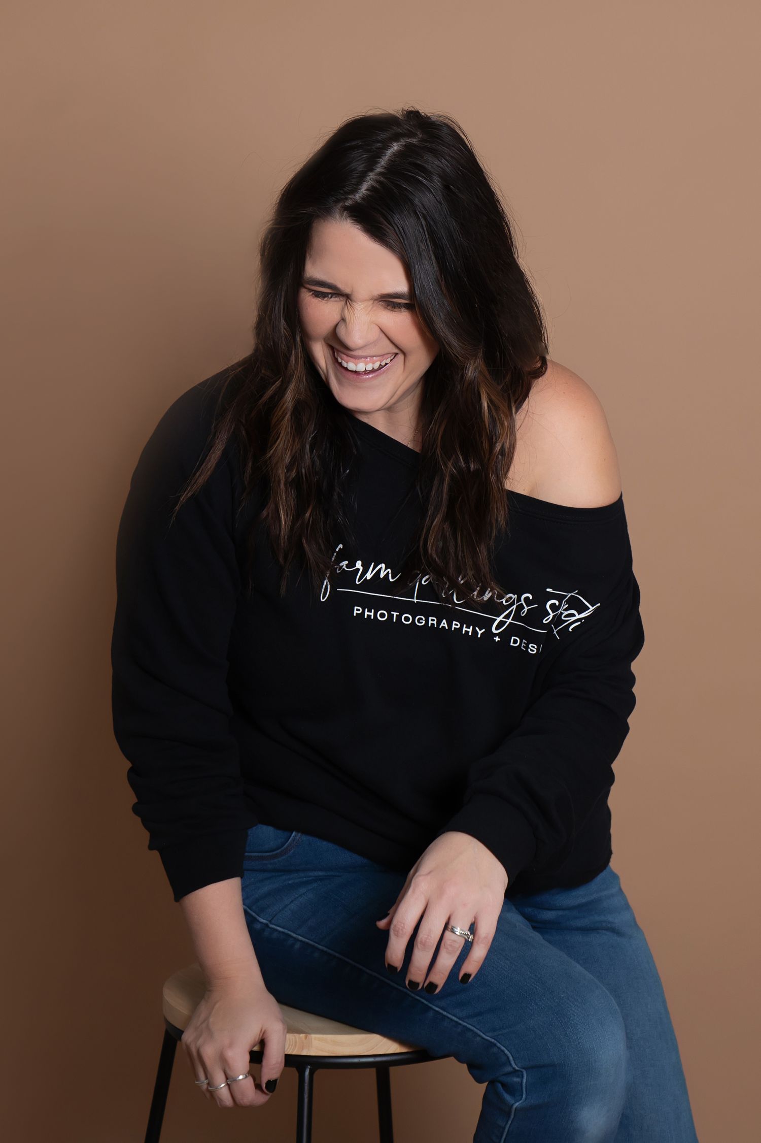 Professional headshot of someone wearing a black photography sweatshirt and jeans while sitting on a stool.