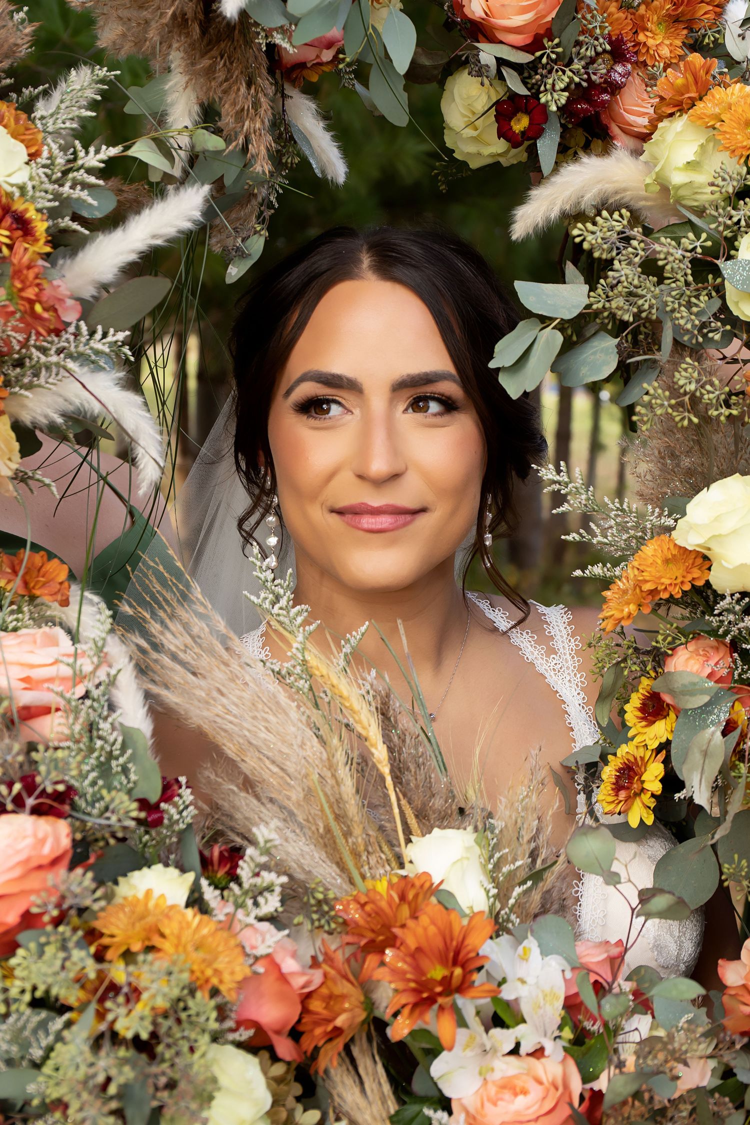 Bridal portrait framed by stunning fall-colored flowers, greenery and pampas grass.