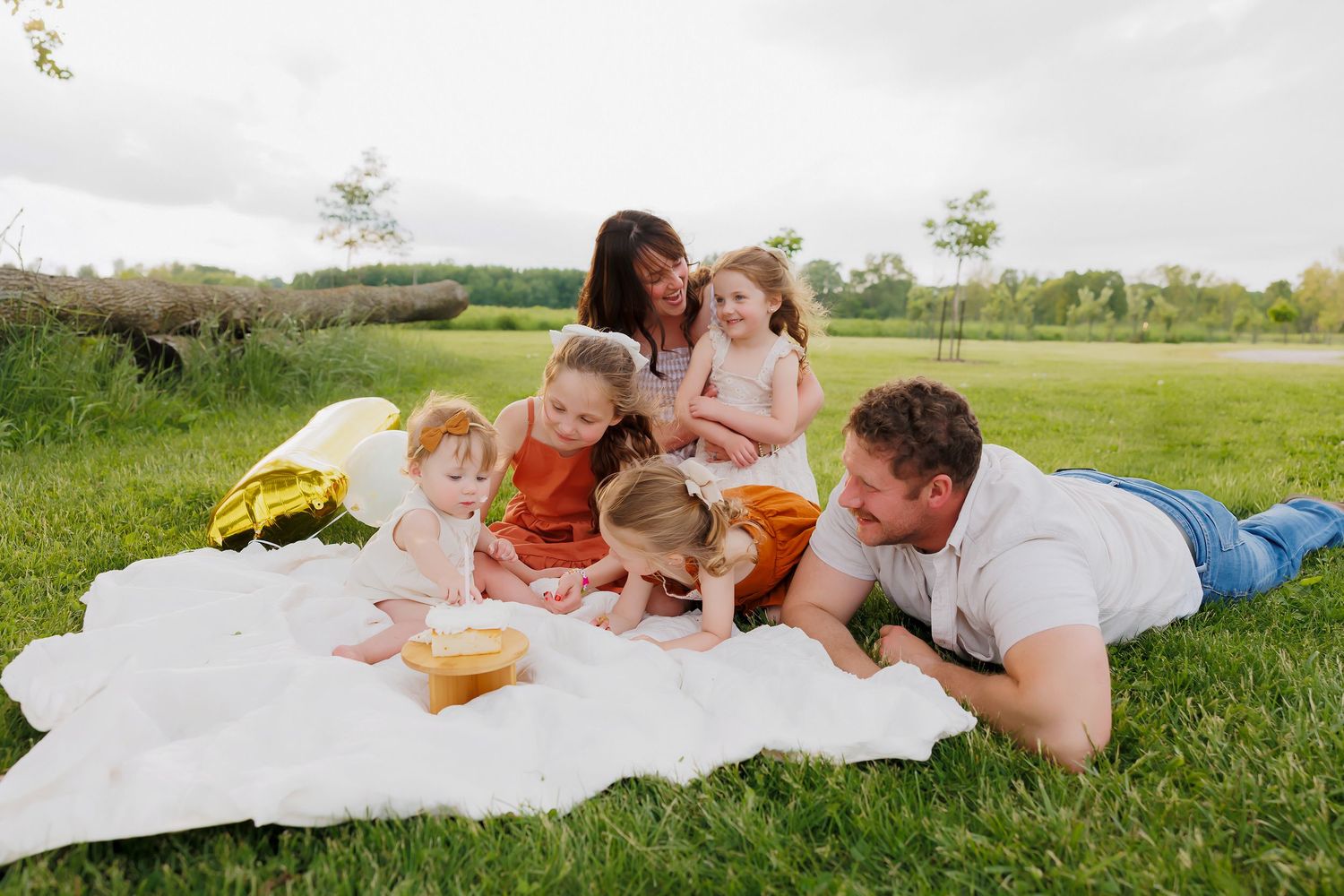 A family enjoys a sunny outdoor picnic together on a white blanket in a grassy field.