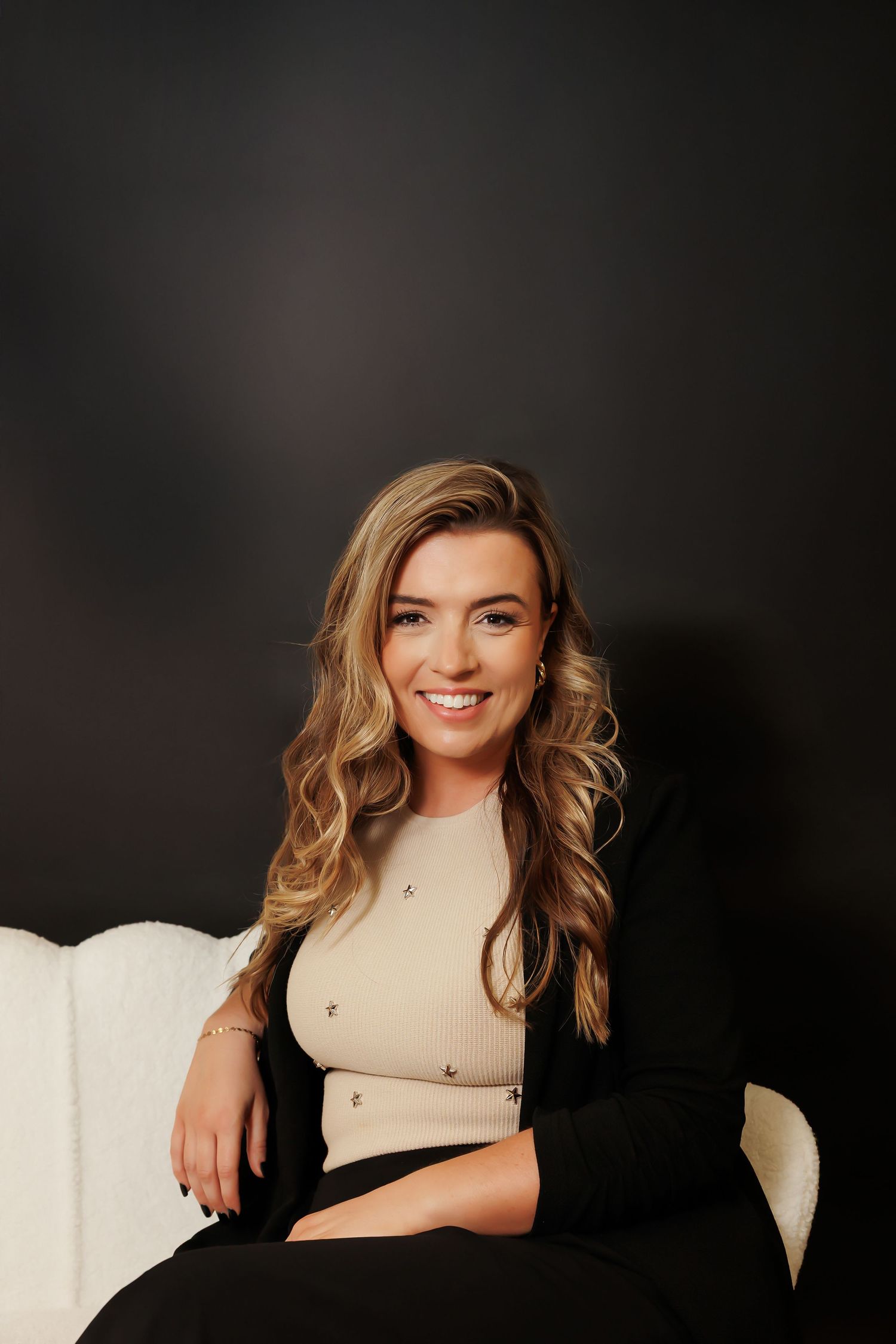 Studio portrait against dark background showing blonde wavy hair and bright smile in professional headshot style.