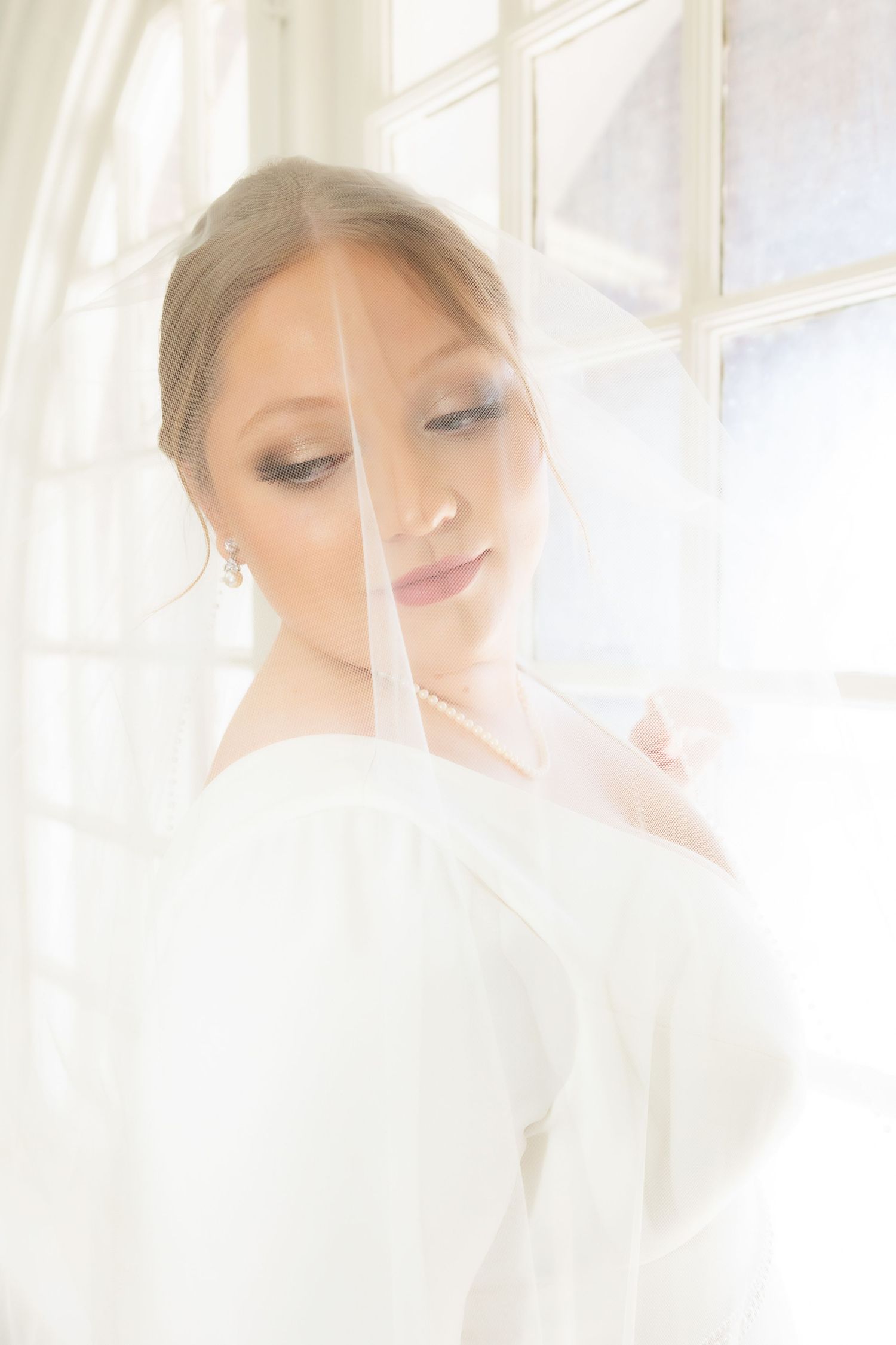A ethereal bridal portrait with soft window light and white tulle creating a dreamy atmosphere.