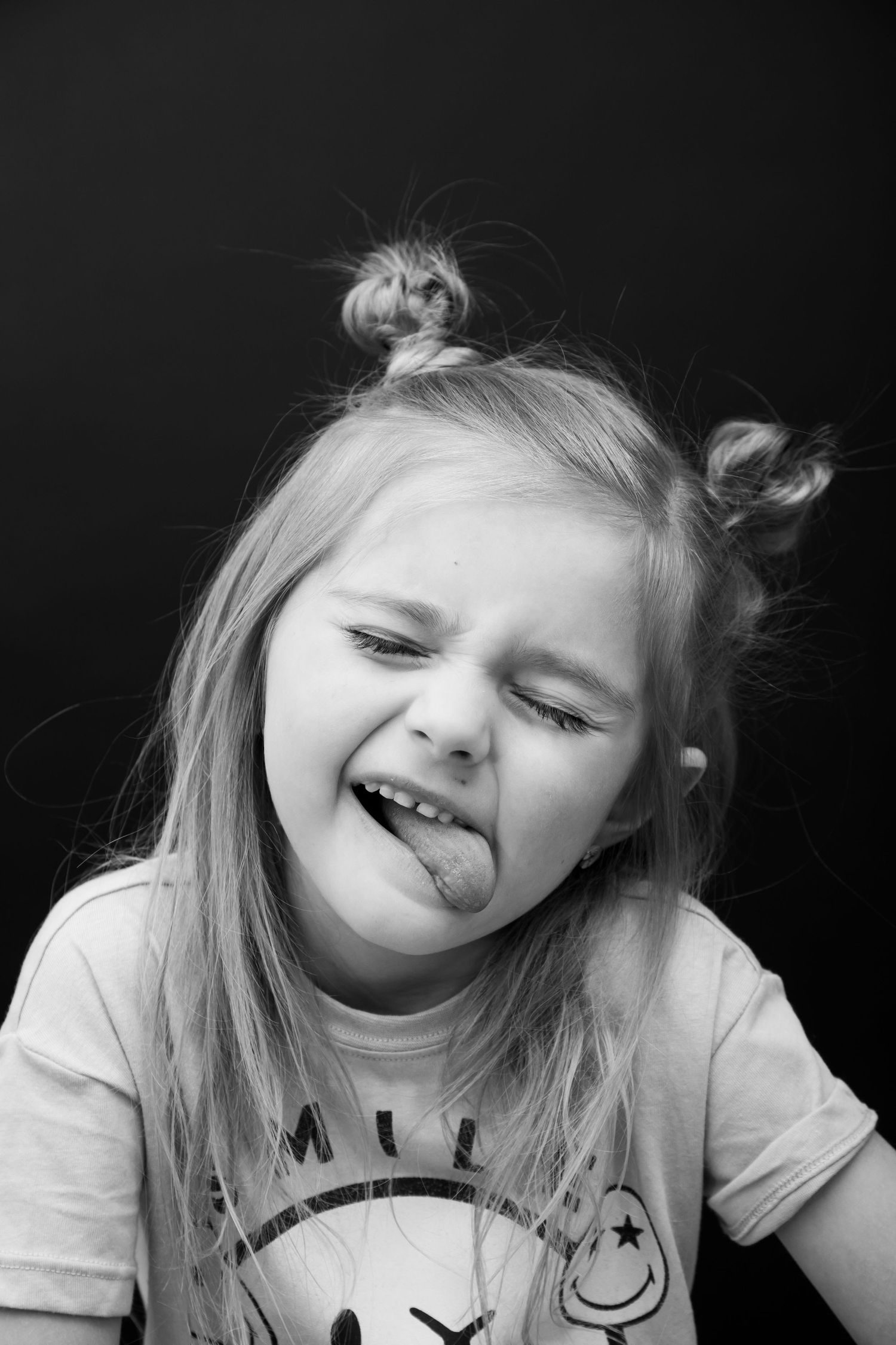 Black and white portrait showing playful expression with messy hair buns.