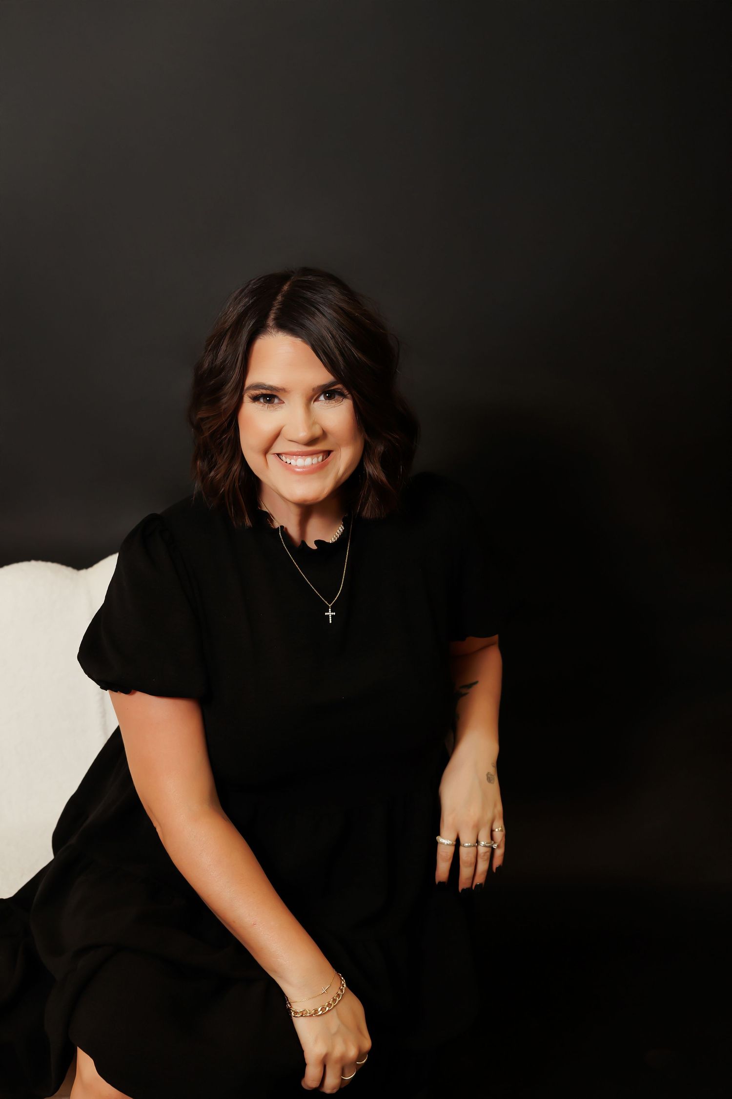 Professional studio portrait of someone in a black dress against a dark background, smiling warmly.