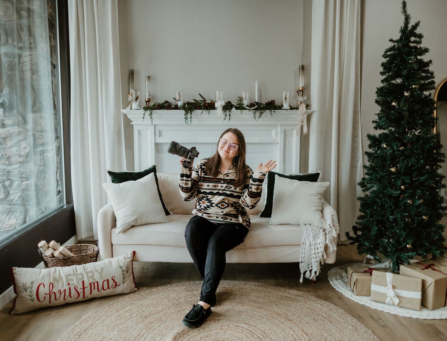 Holiday scene with camera and Christmas tree by white couch with decorative pillows.