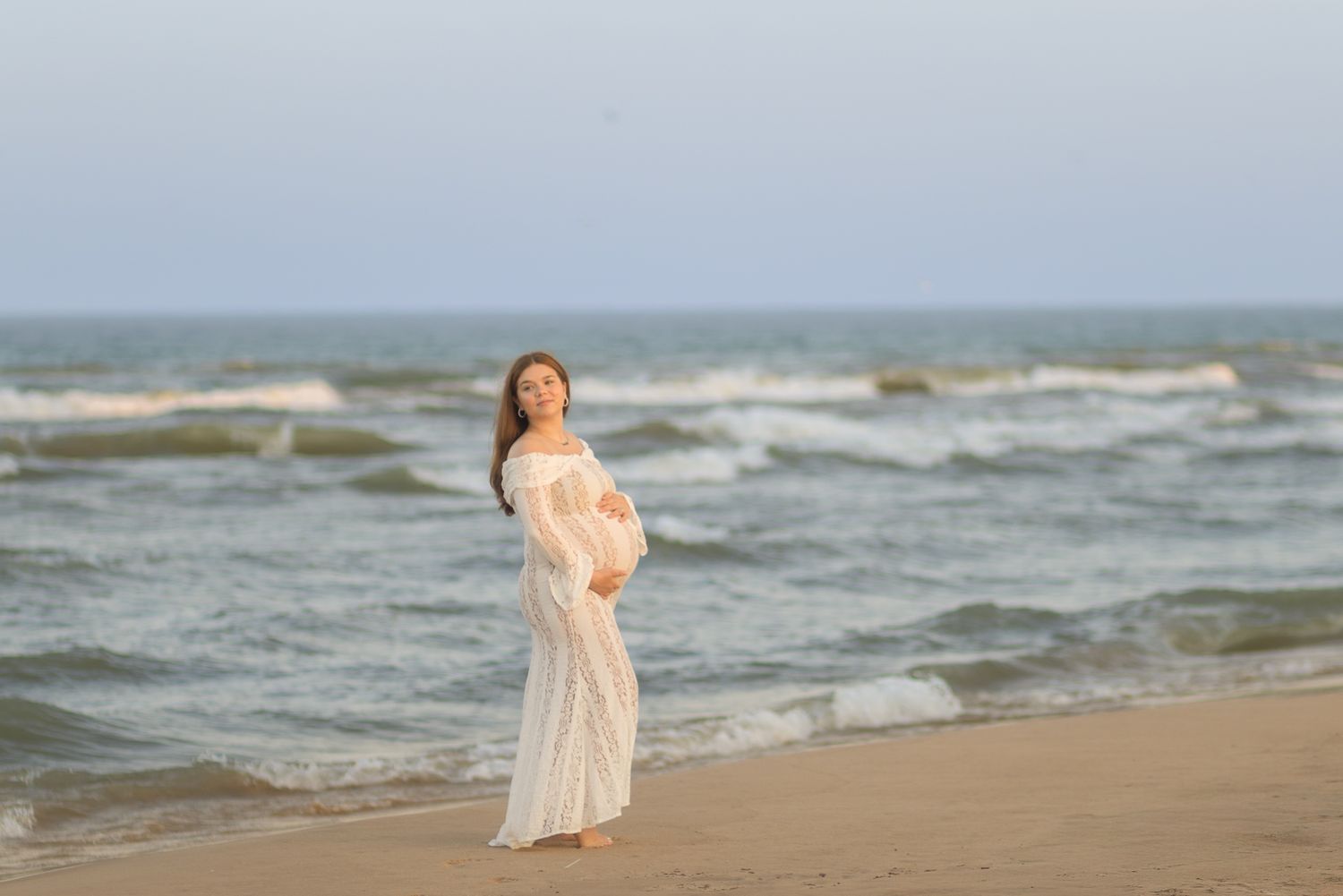 A figure in a flowing white dress walks along a beach shoreline in Indiana during golden hour.