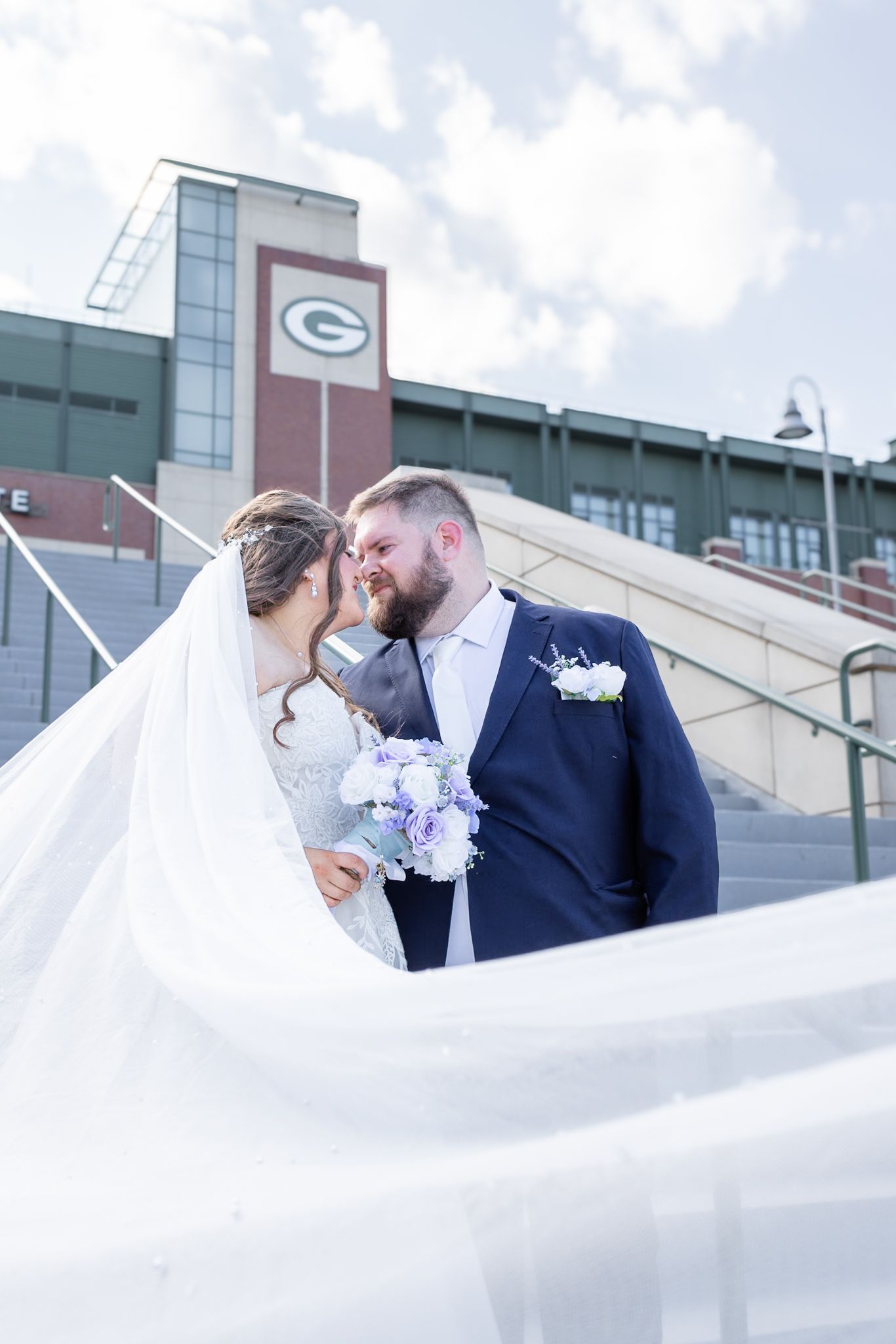 Wedding photo at Lambeau Field stadium with couple and purple bouquet.