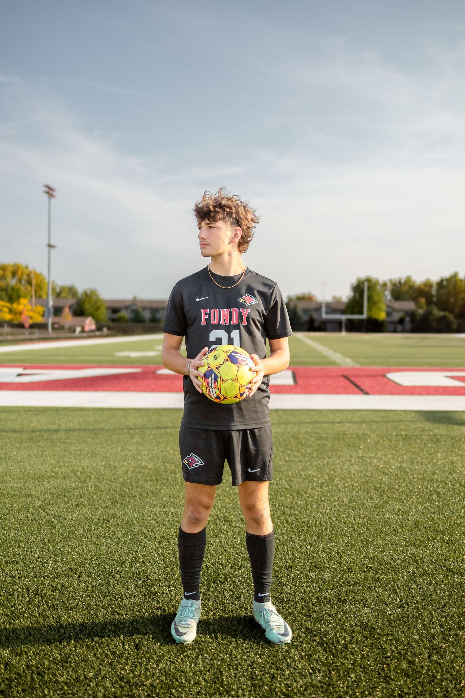 Soccer player in black uniform holding yellow ball on turf field.