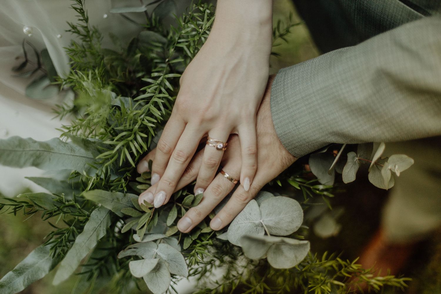 Hands arrange fresh evergreen sprigs and white flowers into a floral arrangement on a wooden surface.