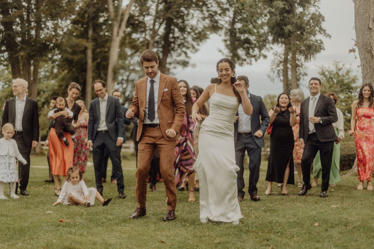 Wedding party walks together across a grassy lawn during an outdoor summer celebration.