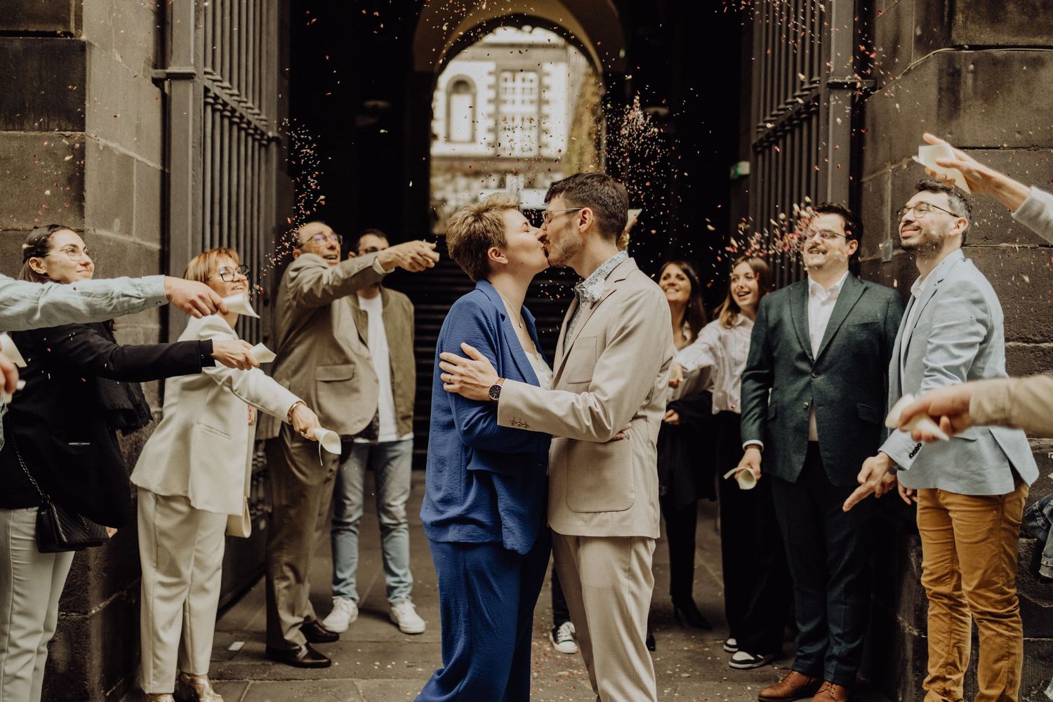 Wedding party members embrace and celebrate in a candid moment outside a historic stone building.